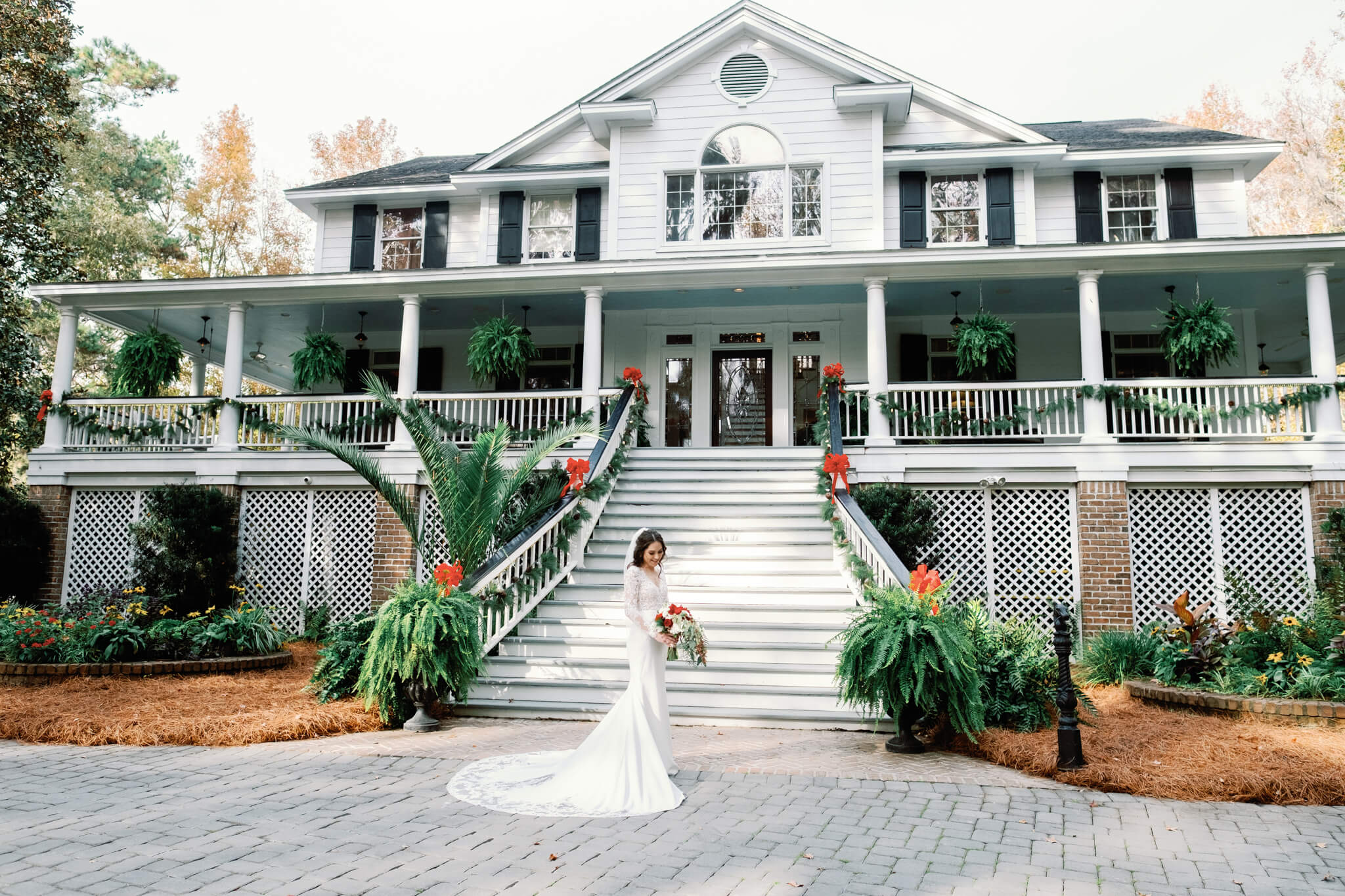 Beautiful bride holding a bouquet of red flowers in front a stunning mansion in Savannah GA