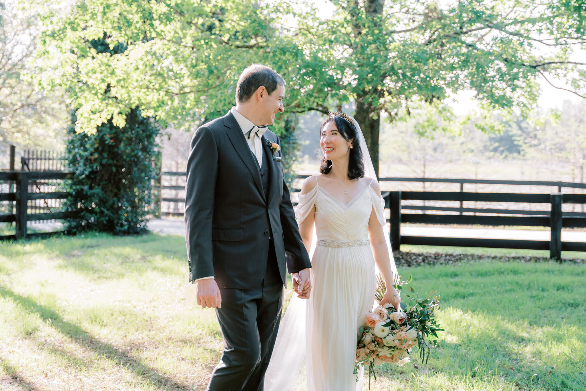 Bride and groom walking hand in hand while smiling at each other during wedding photos at Club Lake venue