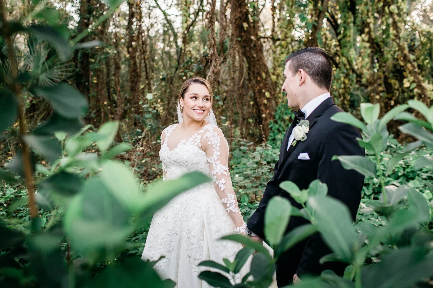 Bride looks at groom while holding hands and walking through a lush garden at Baker's Ranch Wedding Venue