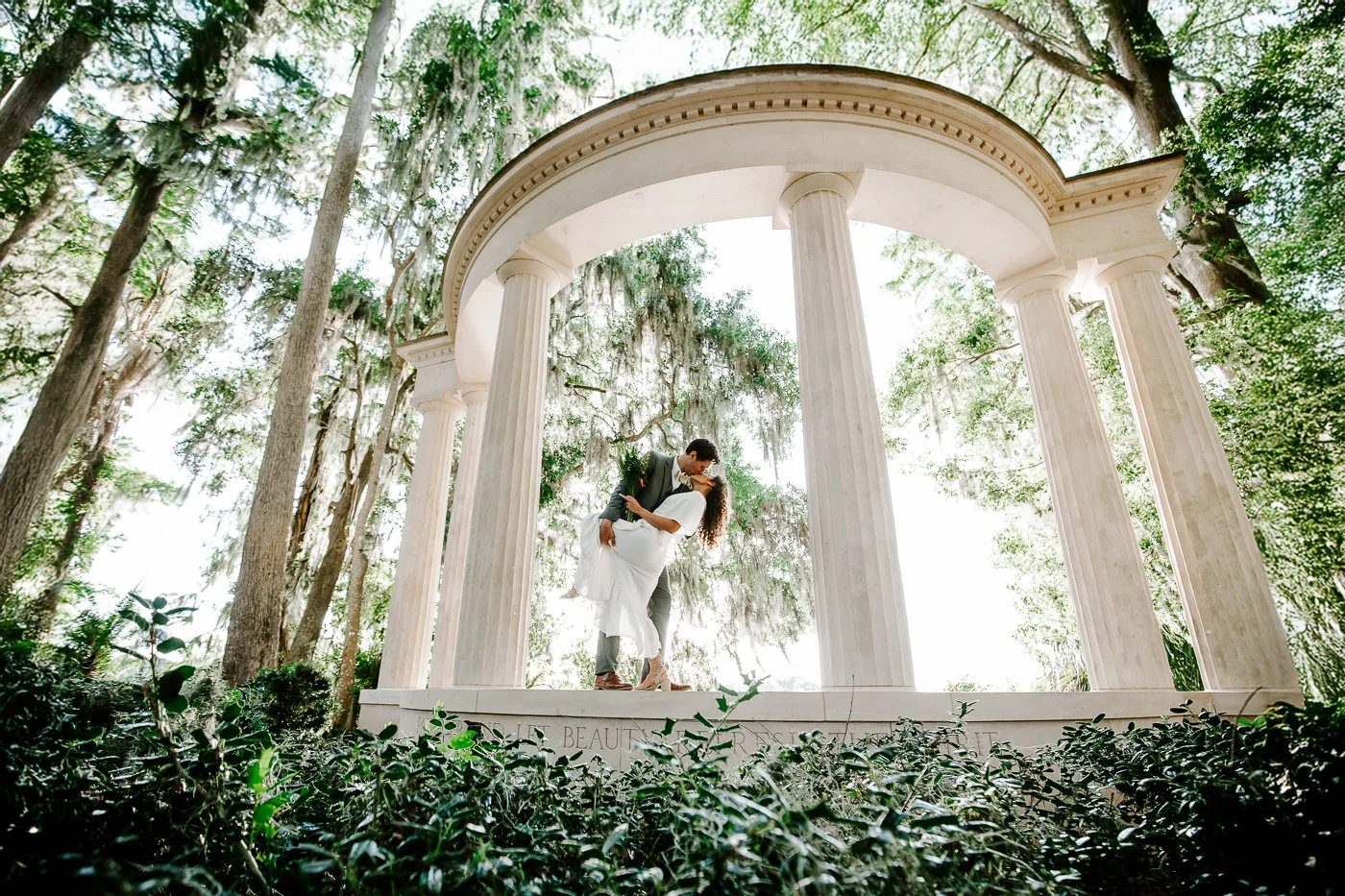 Groom dips the bride while standing in between pillars that resemble Greek or Roman architecture during an elopement at Kraft Azalea Garden in Winter Park, FL