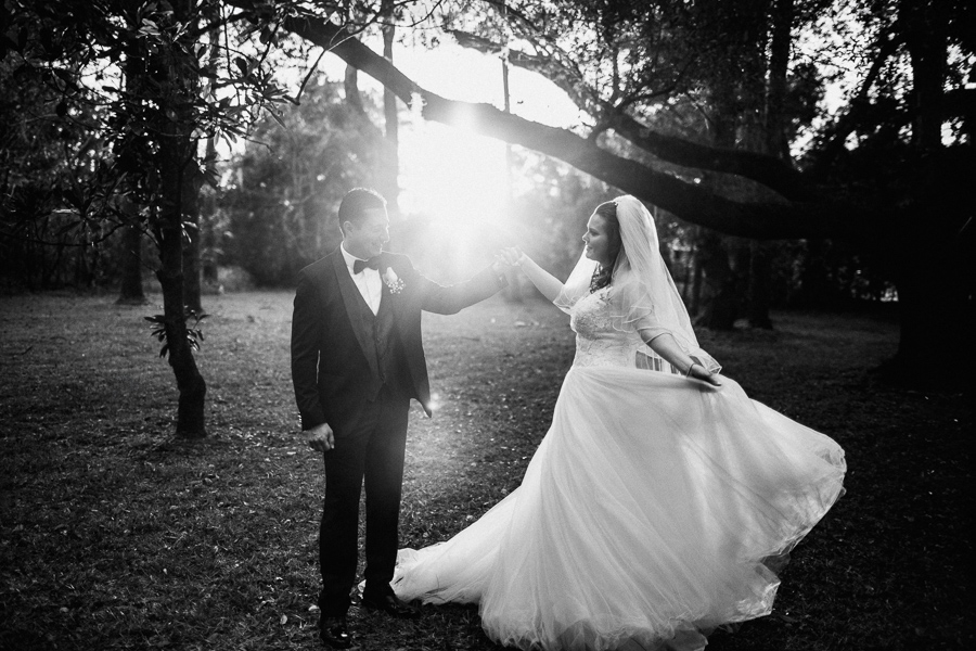 Groom holds bride's hand as she twirls her wedding dress in a garden with glowing sunlight at The Garden Villa wedding venue