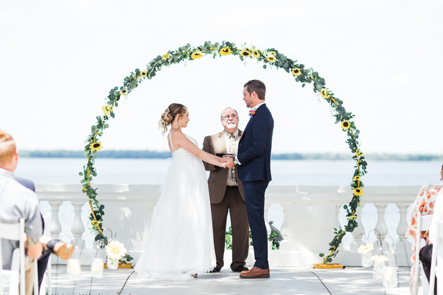 bride and groom holding hands during ceremony under flower arch at a Florida wedding venue