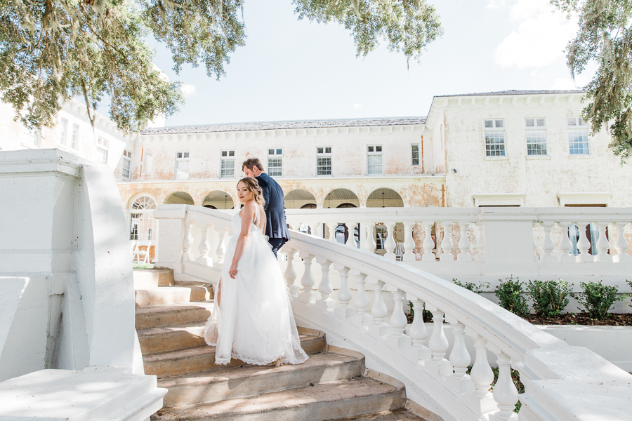 Bride looks back as she and the groom walk up a grand staircase at a Florida wedding venue called Bella Cosa