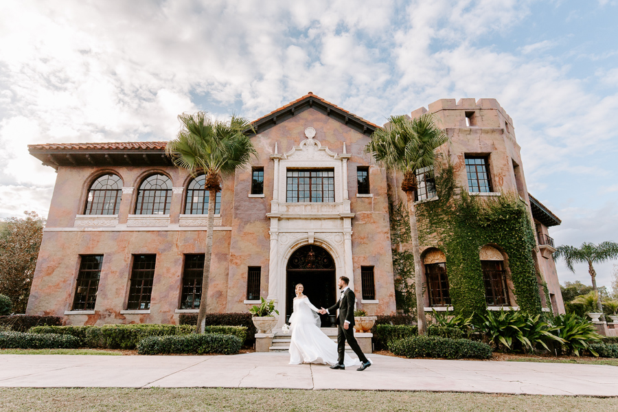 bride and groom walk in front of grand estate mansion at a Florida wedding venue