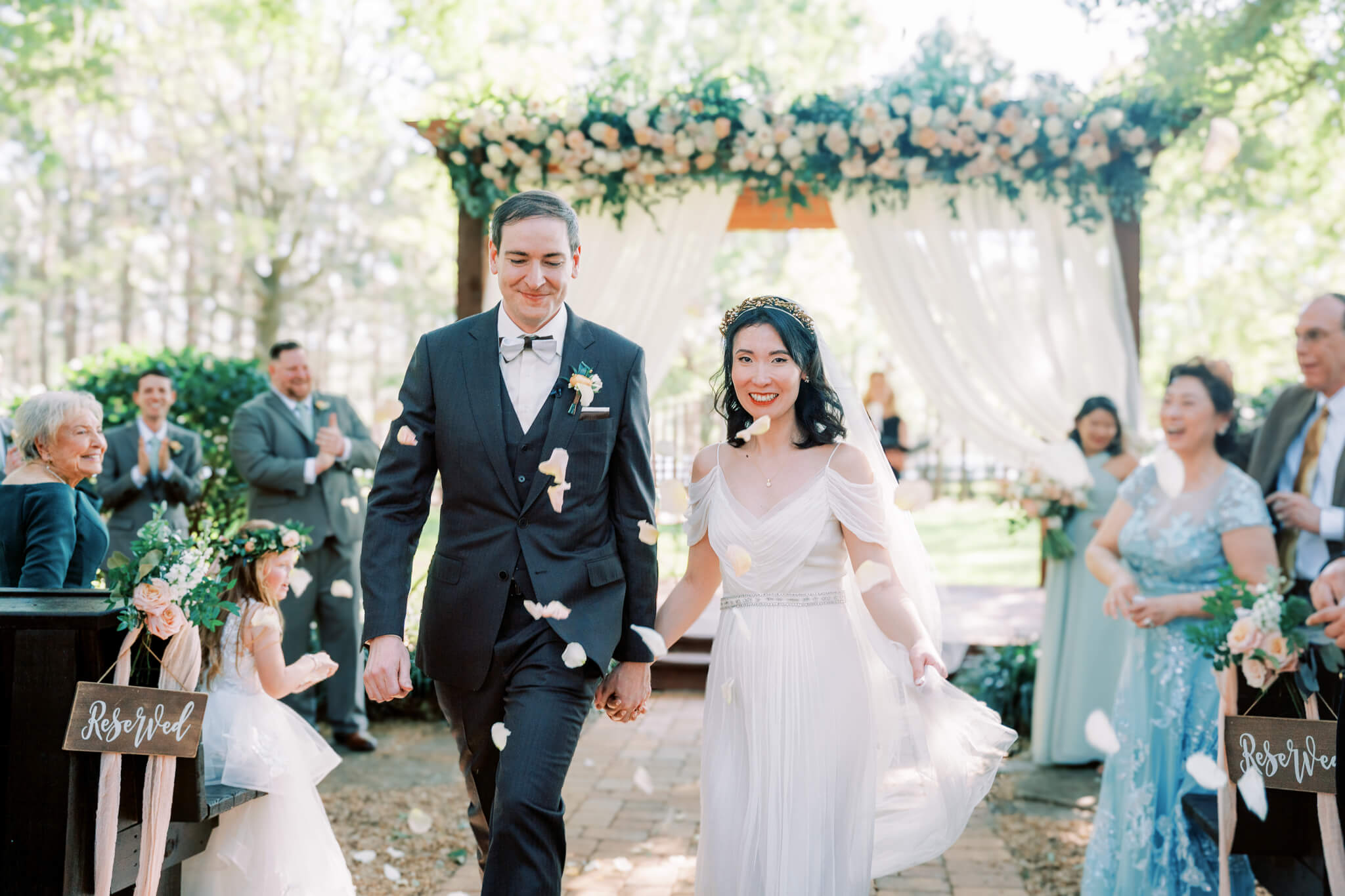 Newlywed couple walk down the isle as guests throw petals at them in celebration