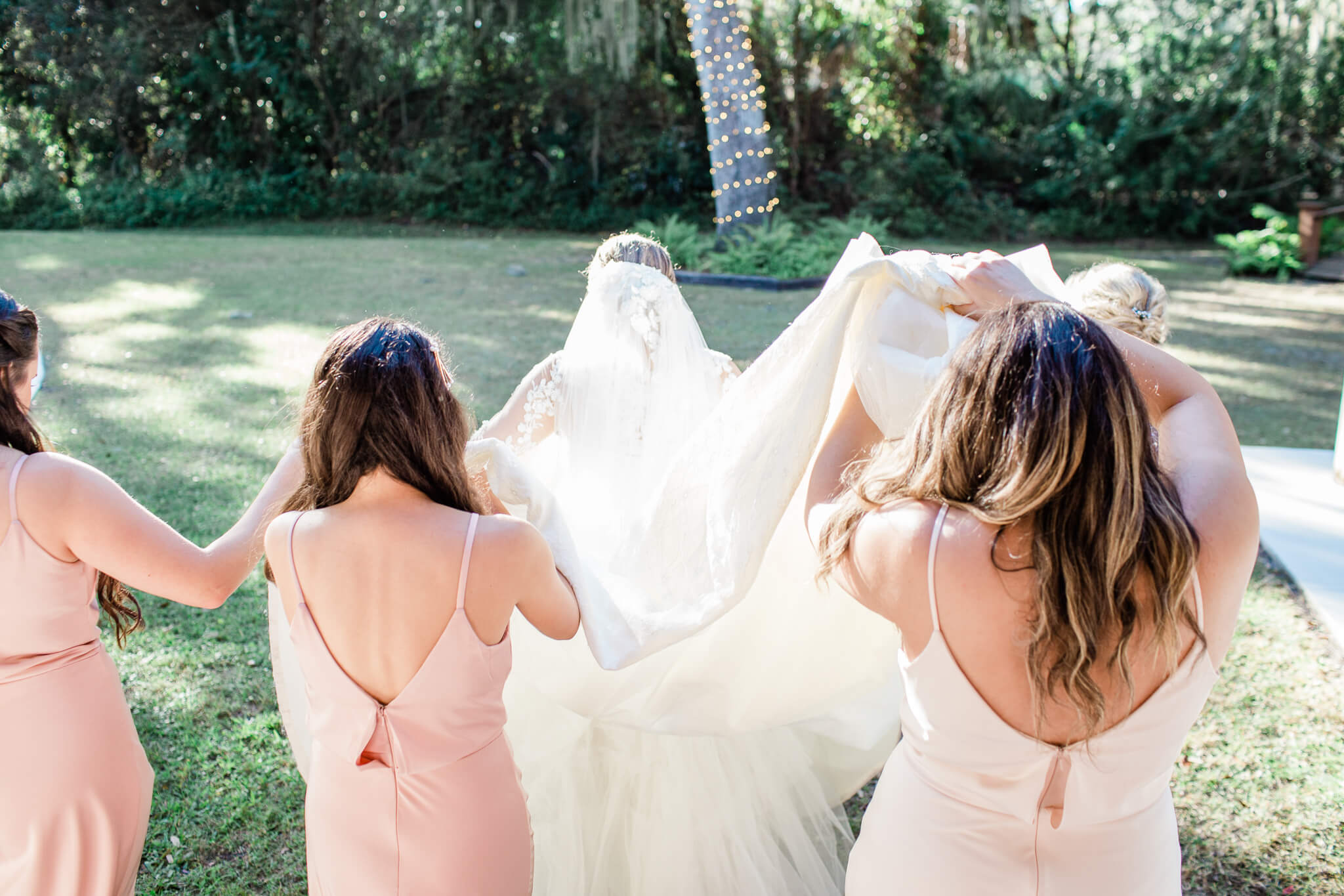 bridesmaids lift and carry the bride's veil as they step outside for wedding photos at Bakers Ranch