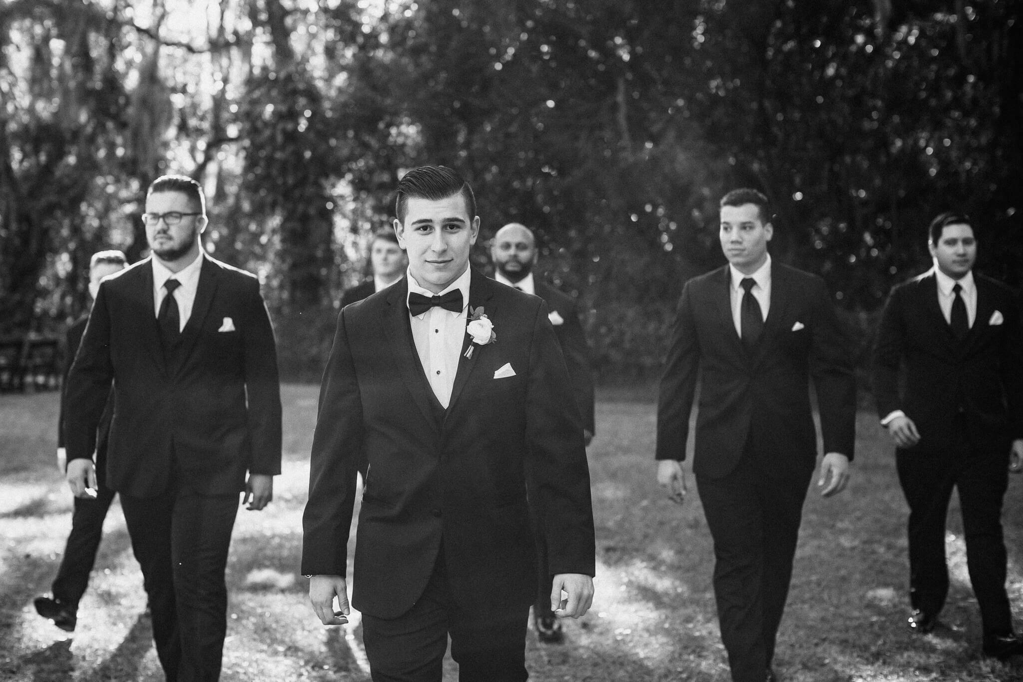 Groom and groomsmen walk in a garden for wedding portraits