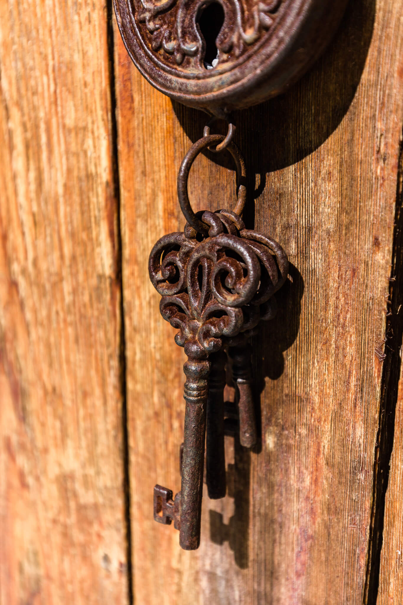 Close up of an iron key hanging from a handle on a rustic wooden door