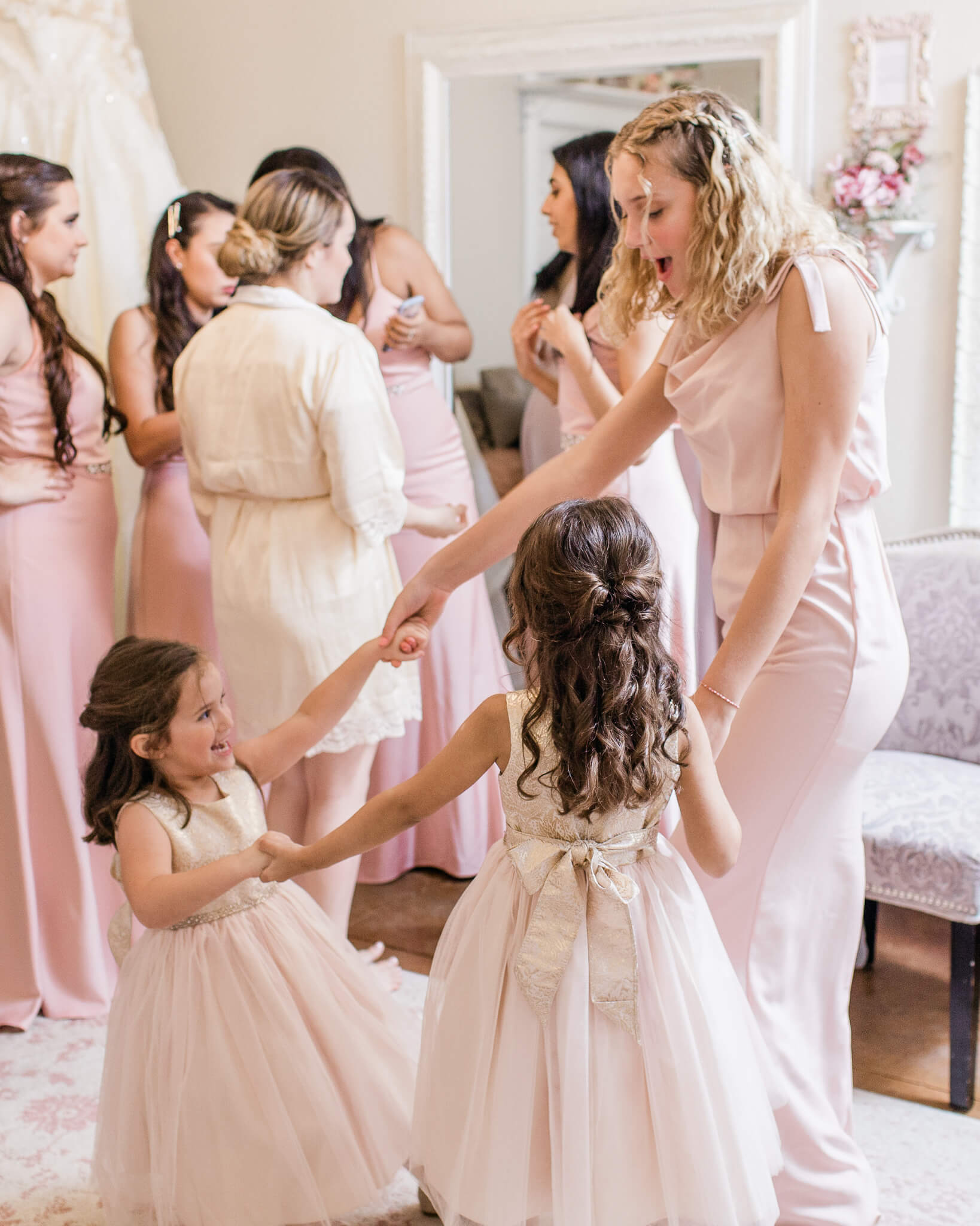 bridesmaid holding hands and playing with flower girls in a bridal suite