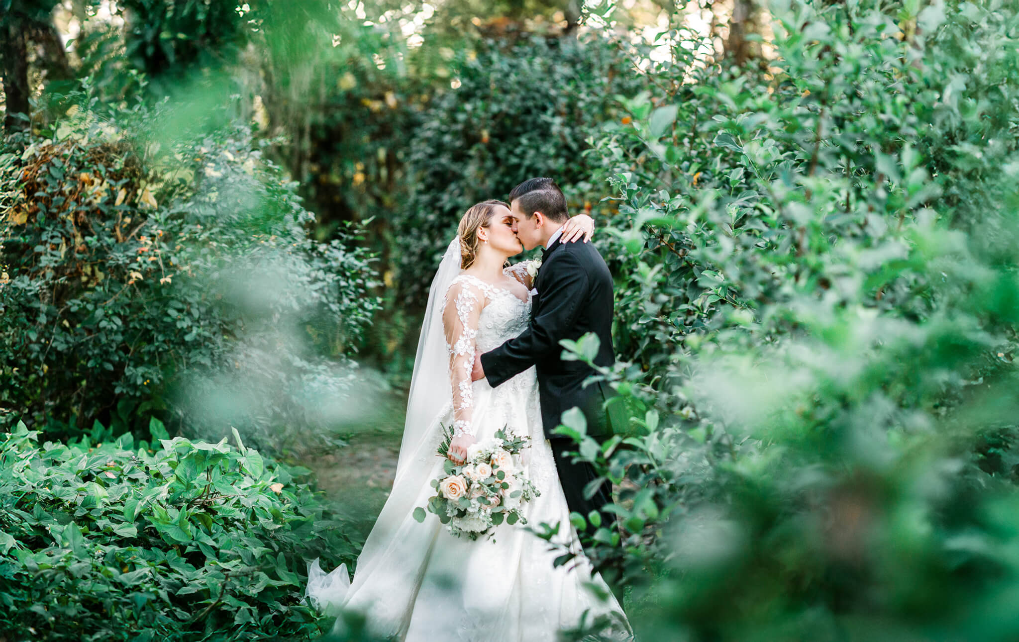 bride and groom kissing in lush garden surrounded by greenery at Bakers Ranch wedding venue
