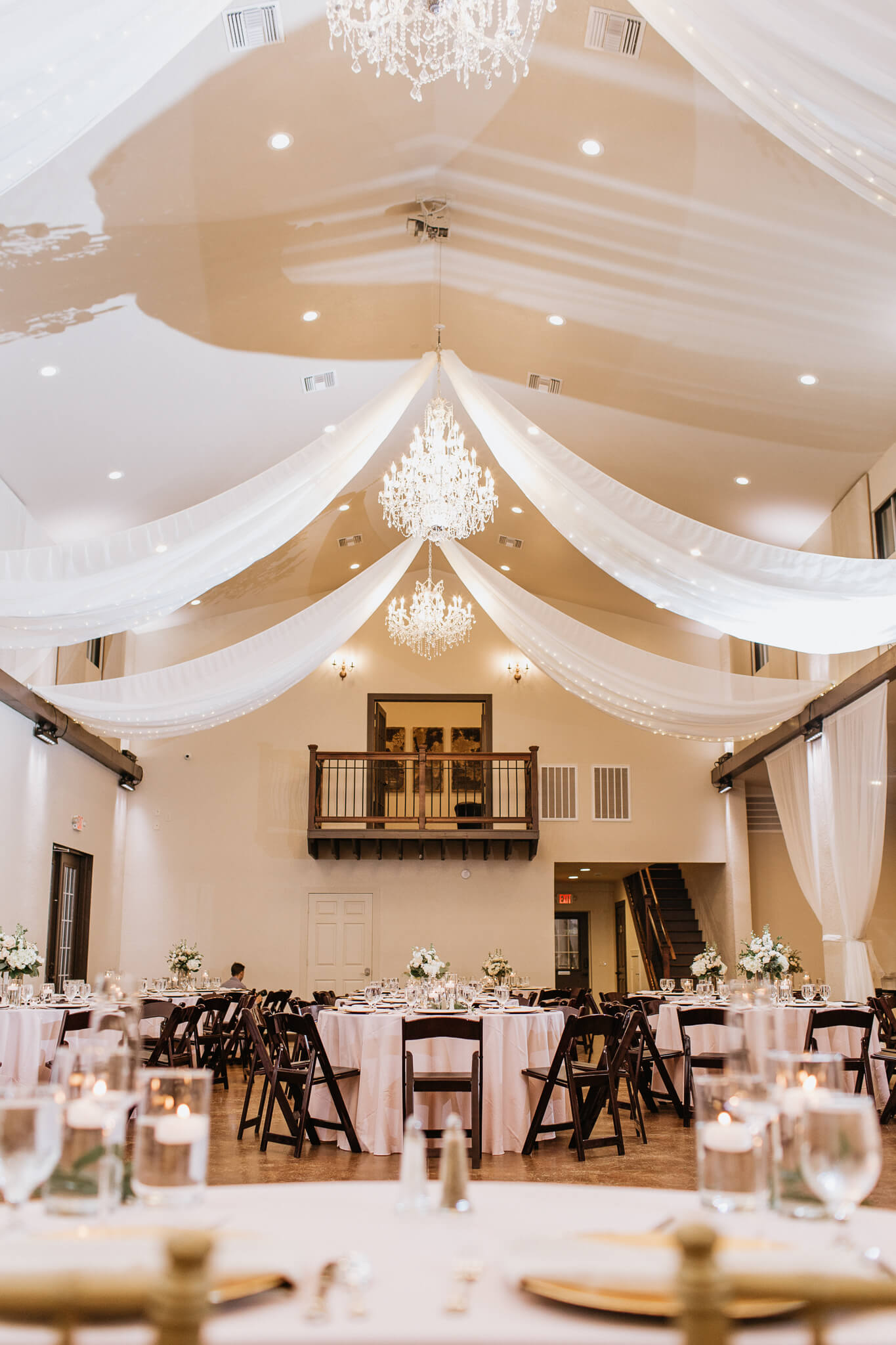 a wedding reception room with drapery and chandeliers