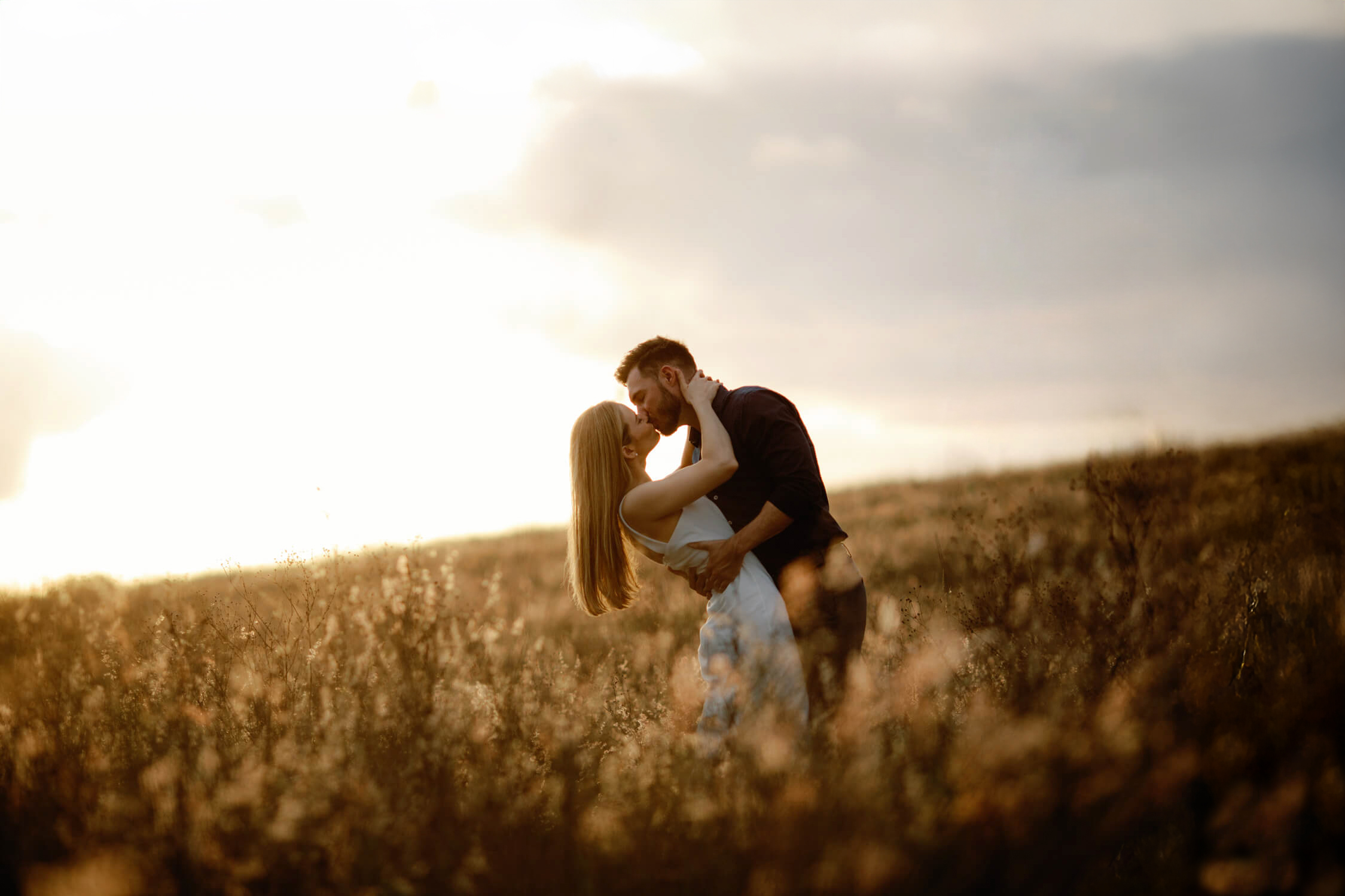 engaged couple embrace with a kiss in a wispy field with golden sunlight at Bok Tower Gardens