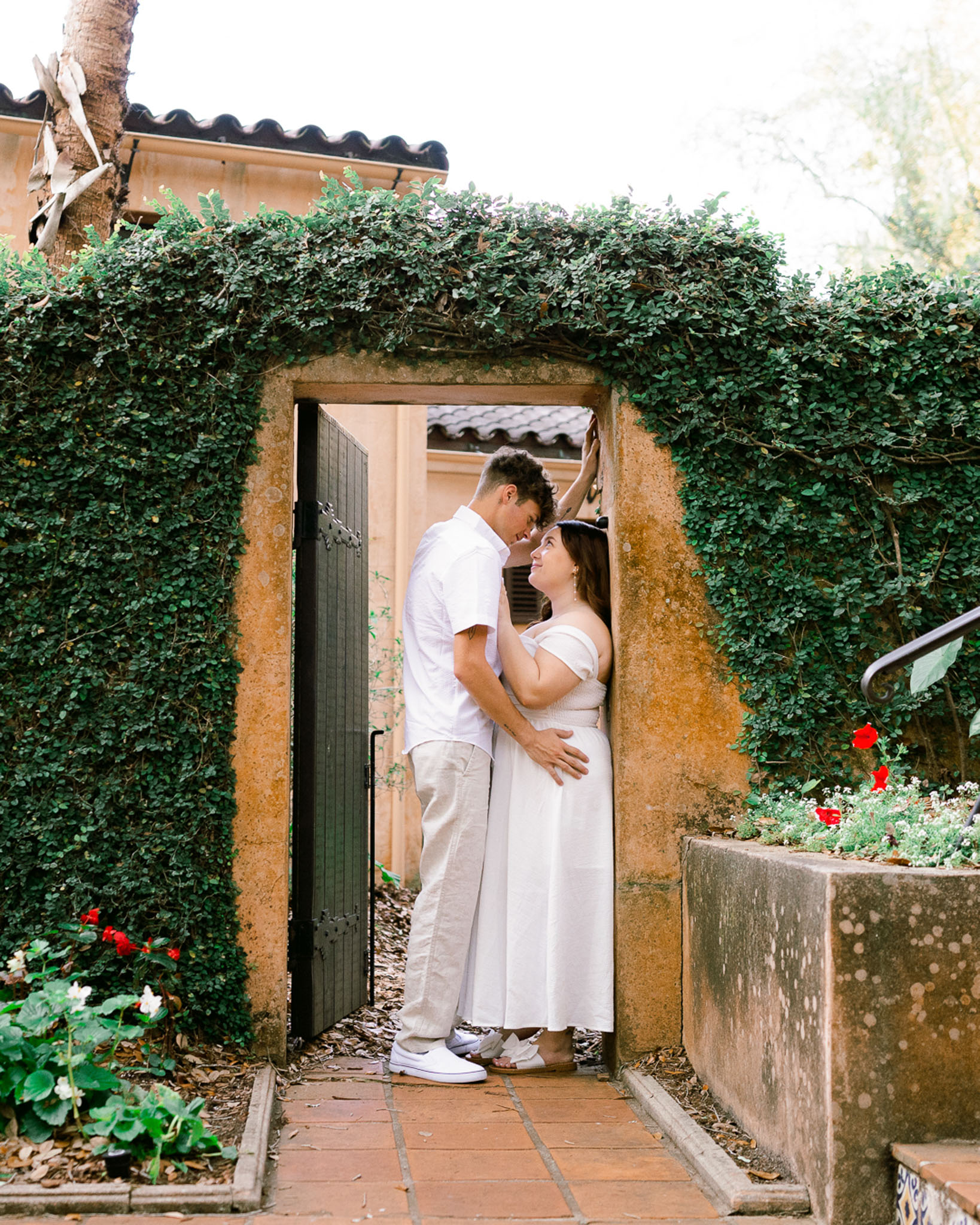 Engaged couple leans into each other under a doorframe covered in green leaves at Bok Tower Gardens