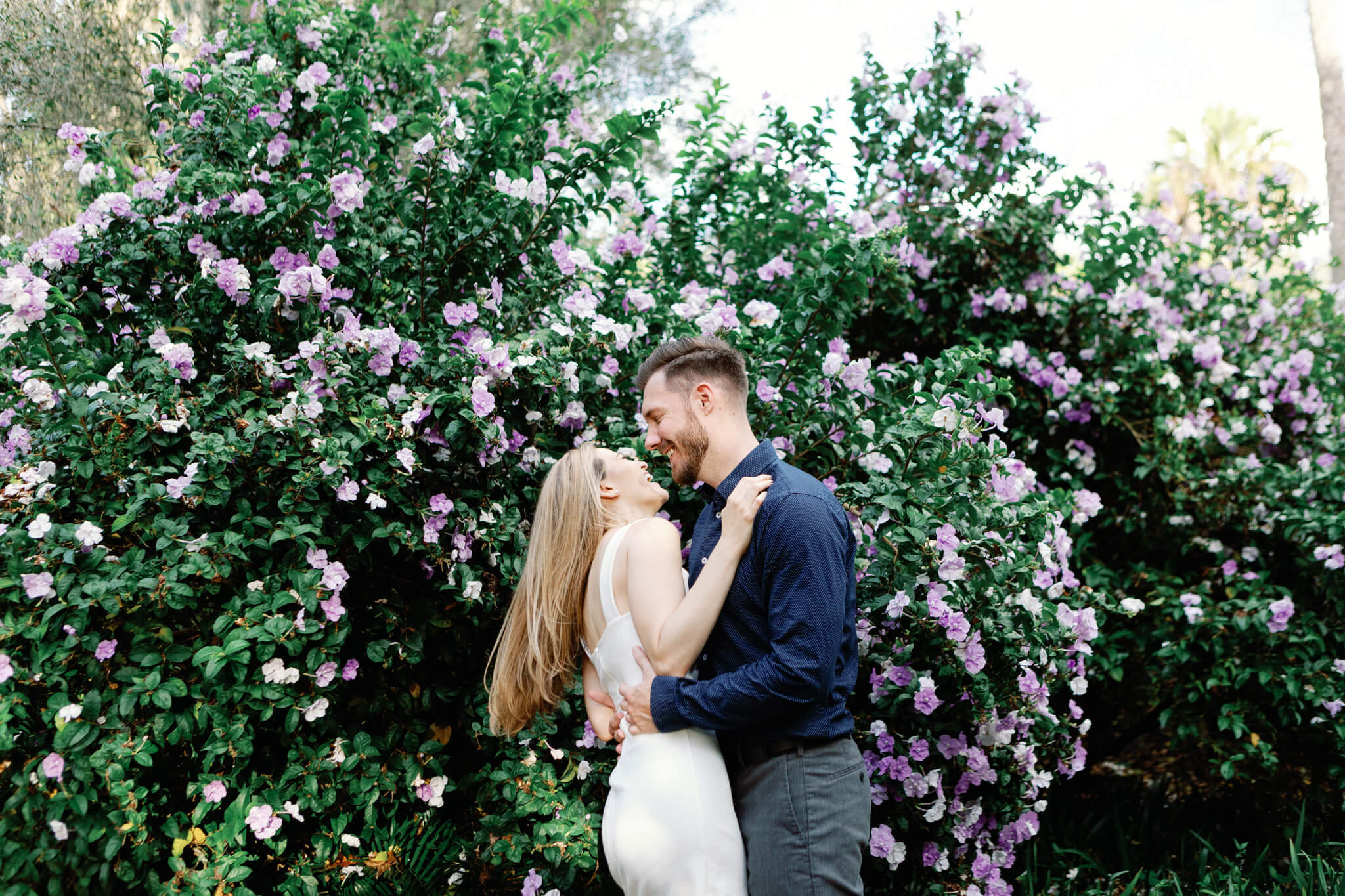 couple posing for engagement photos at Bok Tower Gardens in front of a hedge with flowers