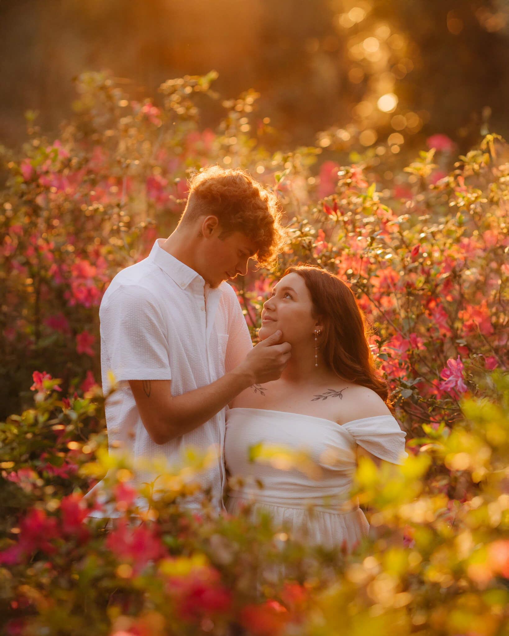 Young couple stands in a dense field with flower during golden hour at engagement session Bok Tower Gardens