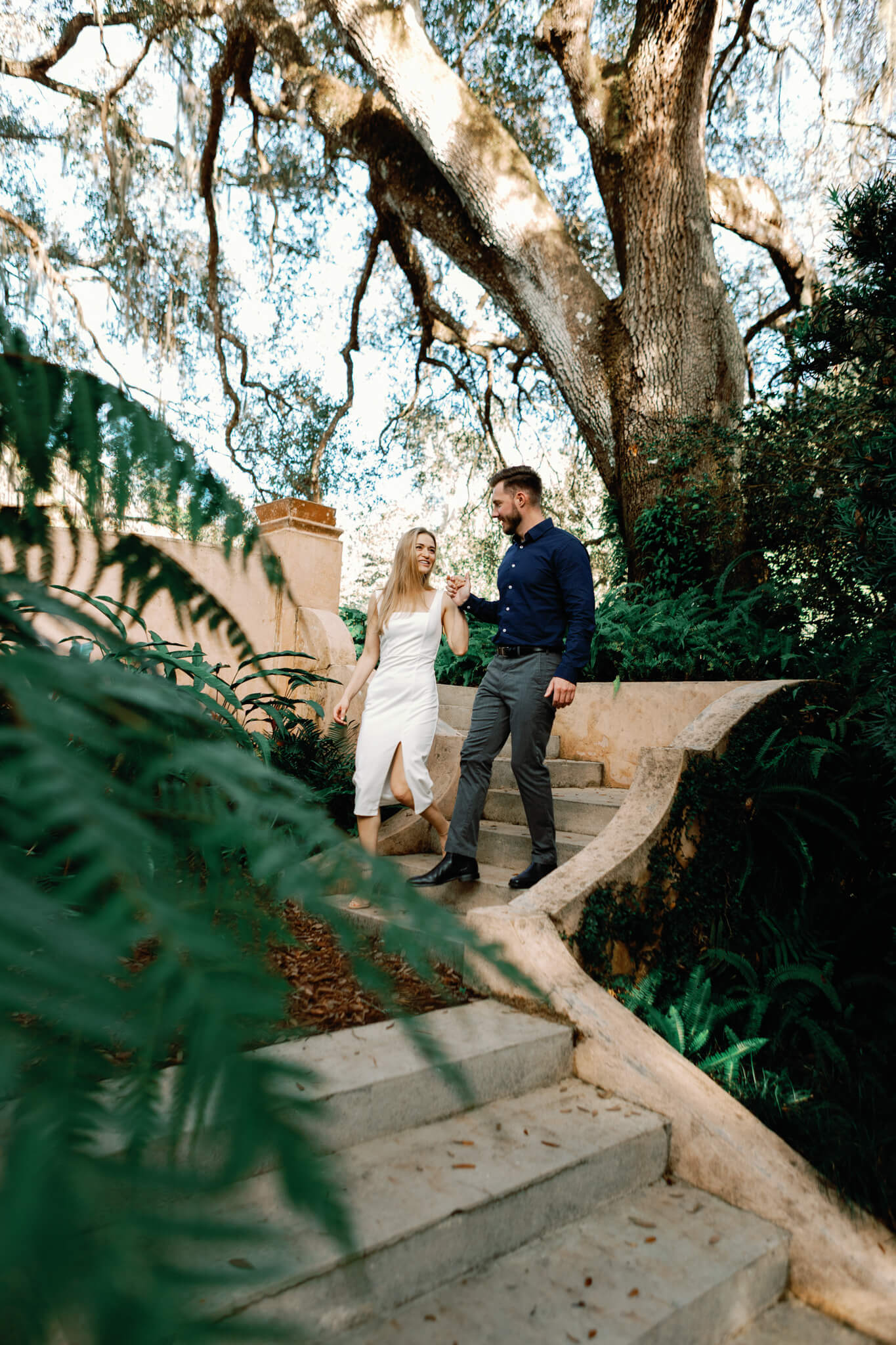 Engaged couple holding hands while they go down a set of stairs in a lush garden