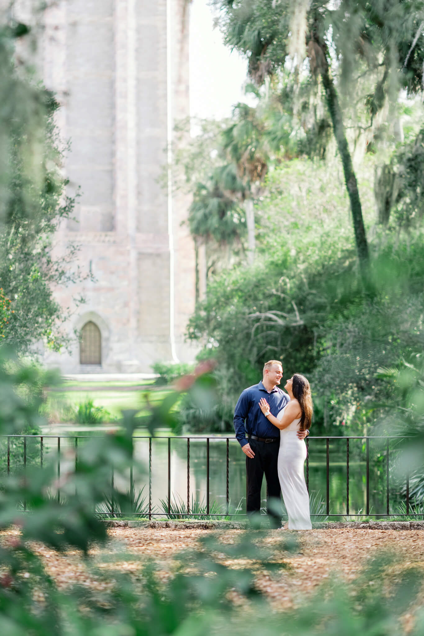 Woman standing close to boyfriend and placing her hand on his chest as they look in to each other with a smile at Bok Tower Gardens for their engagement session