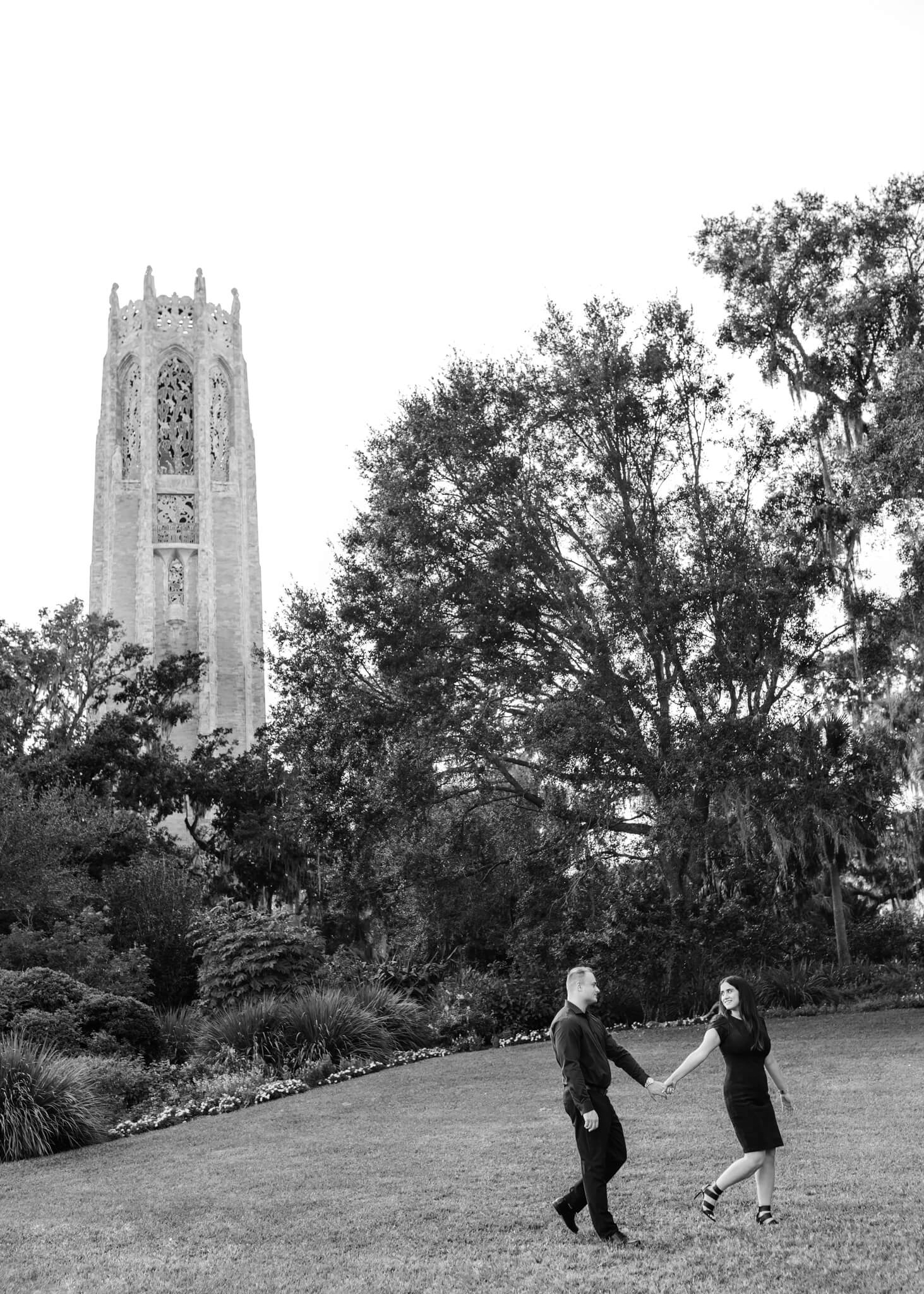 Woman holds man's hand as she looks back at him while posing for engagement photos at Bok Tower Gardens