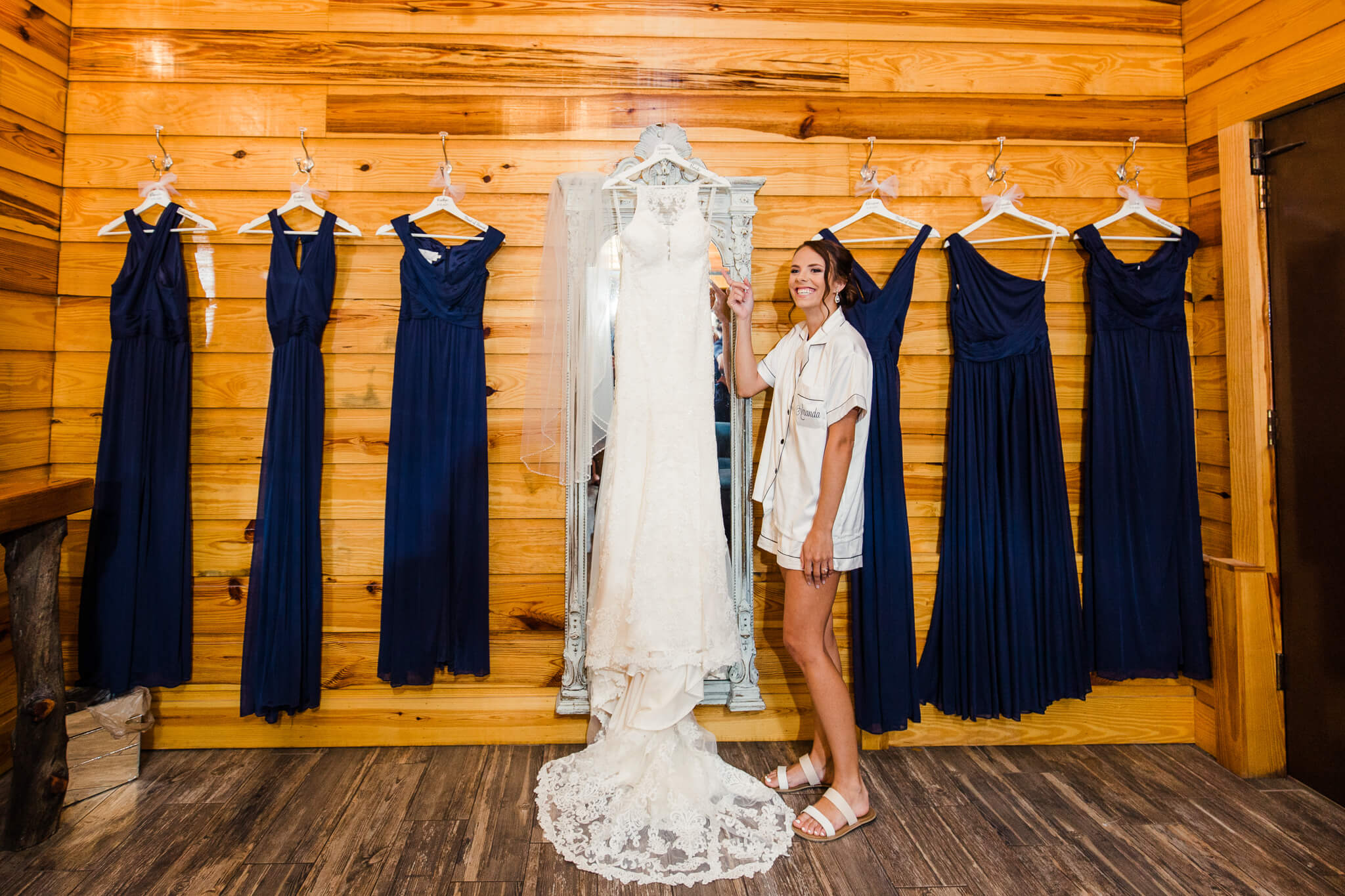 bride stands next to her wedding dress in room with wooden walls for bridal party to get ready at Club Lake Venue
