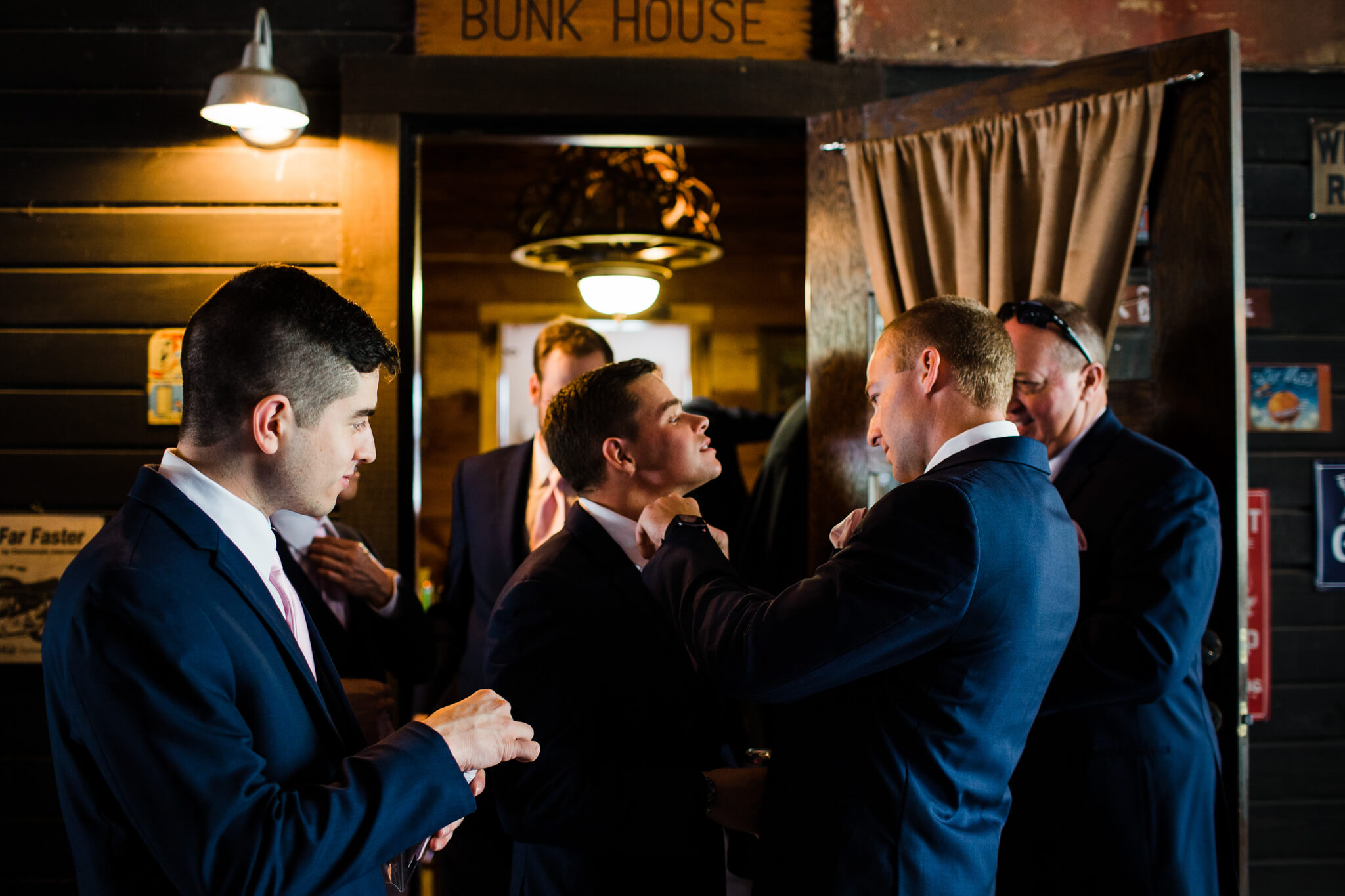 groom adjusts the tie of a groomsan while other groomsmen in blue suits stand around getting ready at an outdoor wedding venue in Orlando