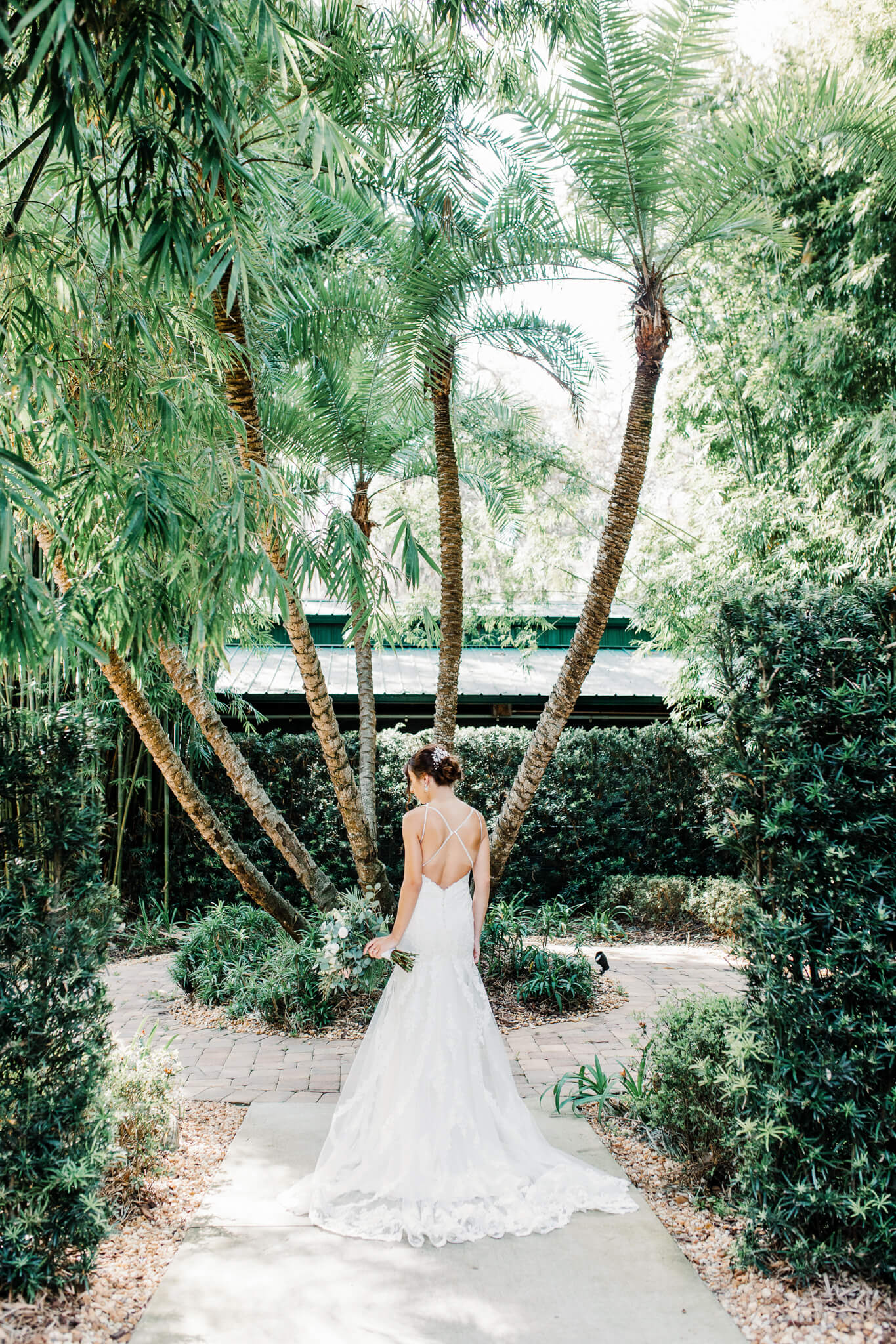 the backside of a bride in a white wedding dress as she holds a gorgeous flower bouquet in a lush courtyard at an outdoor wedding venue in Central FL