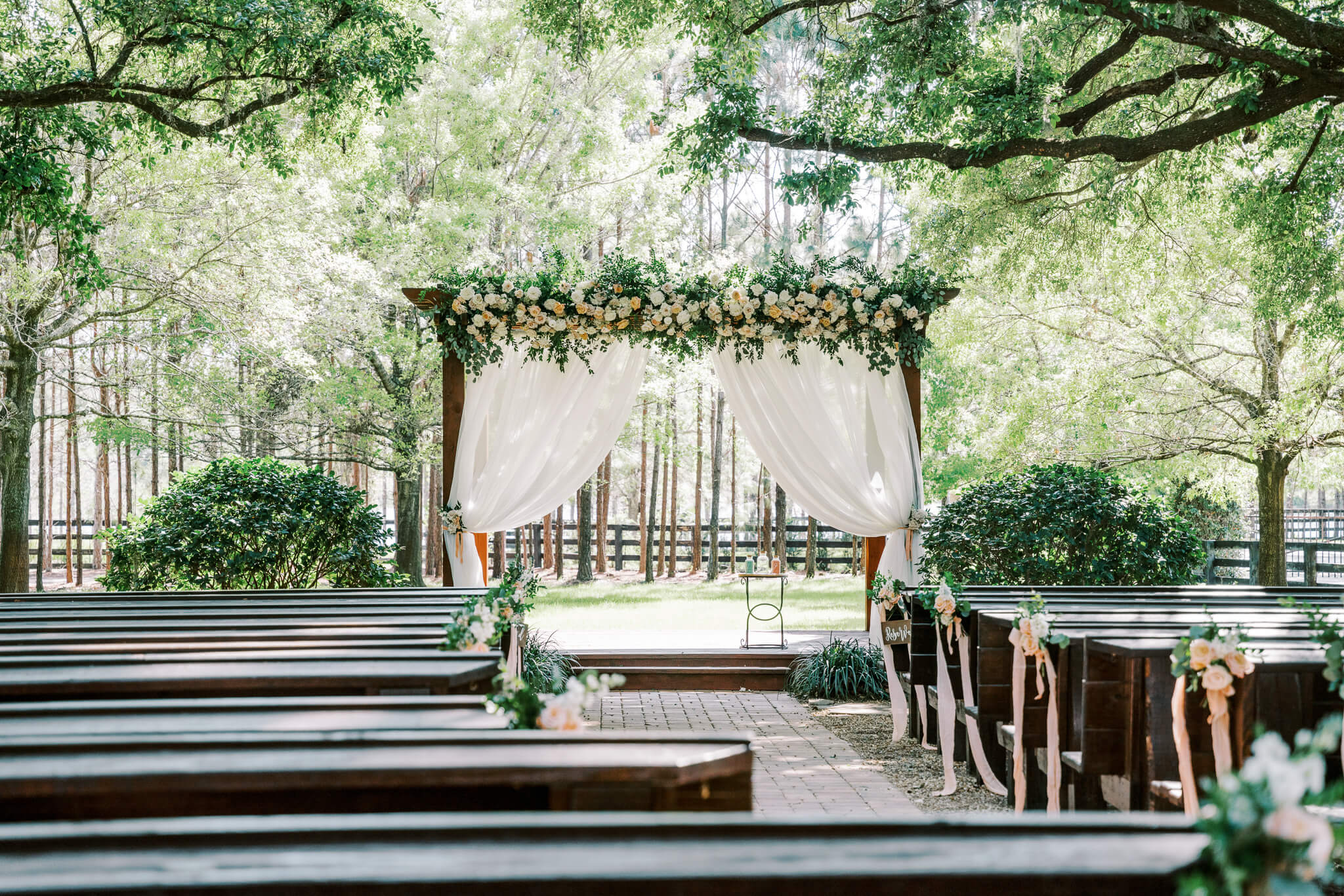 wooden benches in a lush garden for a wedding ceremony underneath a canopy of large oak trees nested in nature