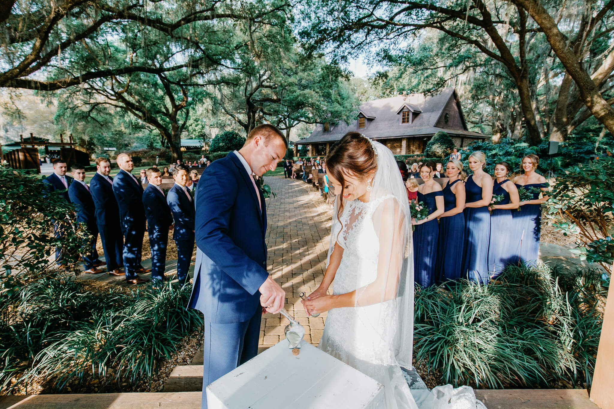 Bride and groom pour sand from different containers into a single container as a ritual that symbolizes their union at an outdoor wedding venue in Central FL