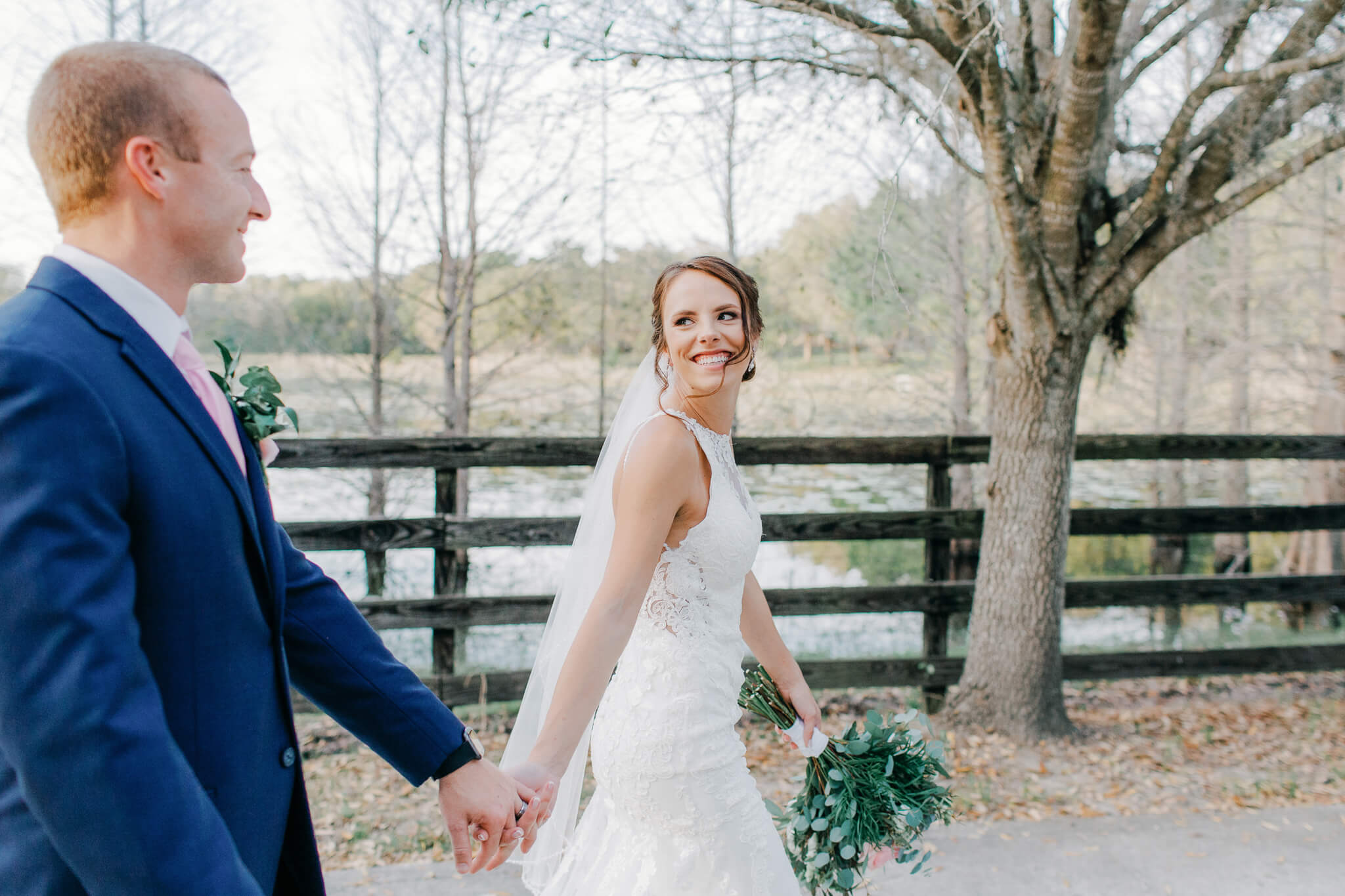 Bride looks back at groom with a smiles as they walk hand in hand at an outdoor wedding venue in Central FL