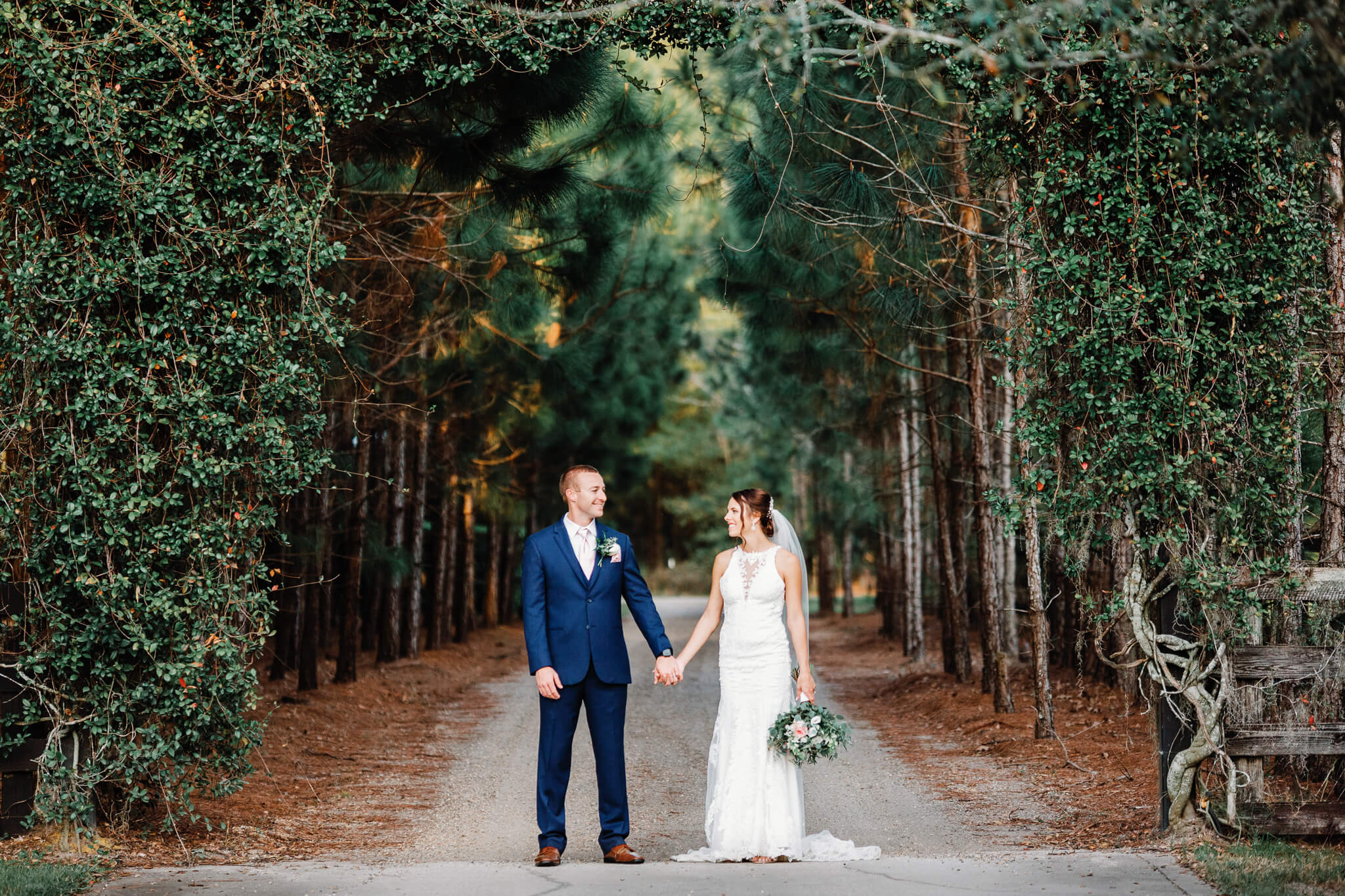 Bride and groom hold hands in front of a bunch of trees