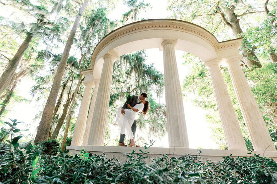 bride and groom kiss and dip on a concrete structure with greek-style pillars in an Orlando wedding venue with lush greenery