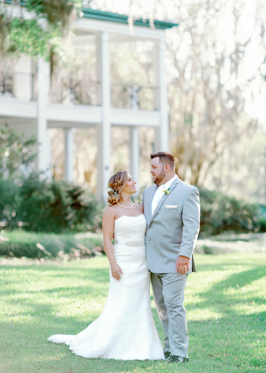 Bride and groom look at each other while posing for portrait in front of a estate mansion in a lush garden at an Orlando wedding venue