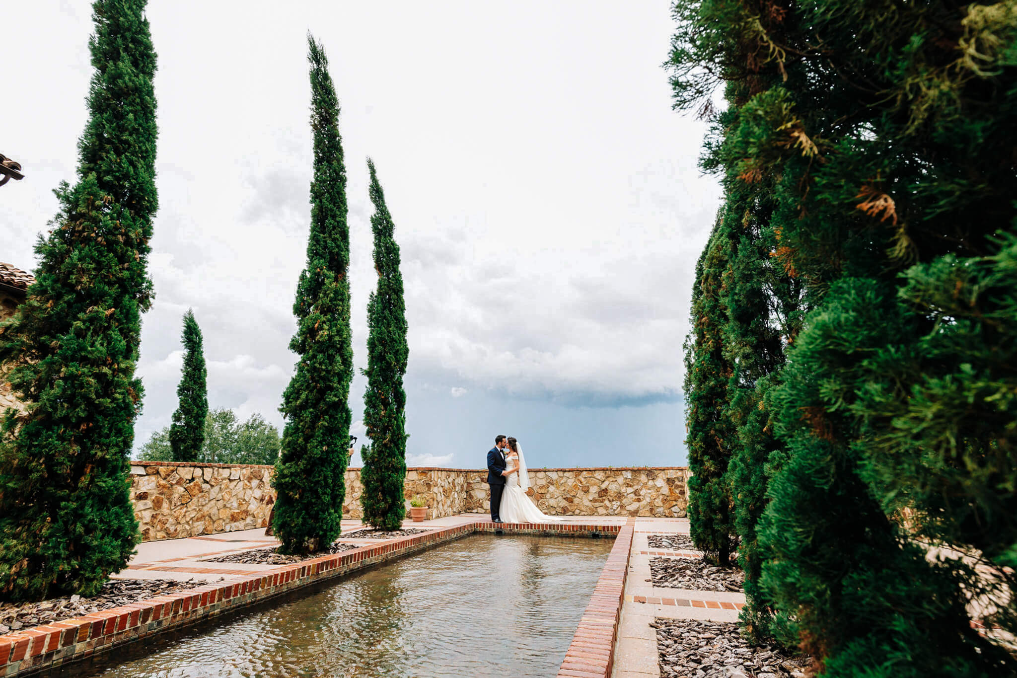 wedding couple embraces with a kiss while standing in front of a fountain during a Florida wedding at Bella Collina