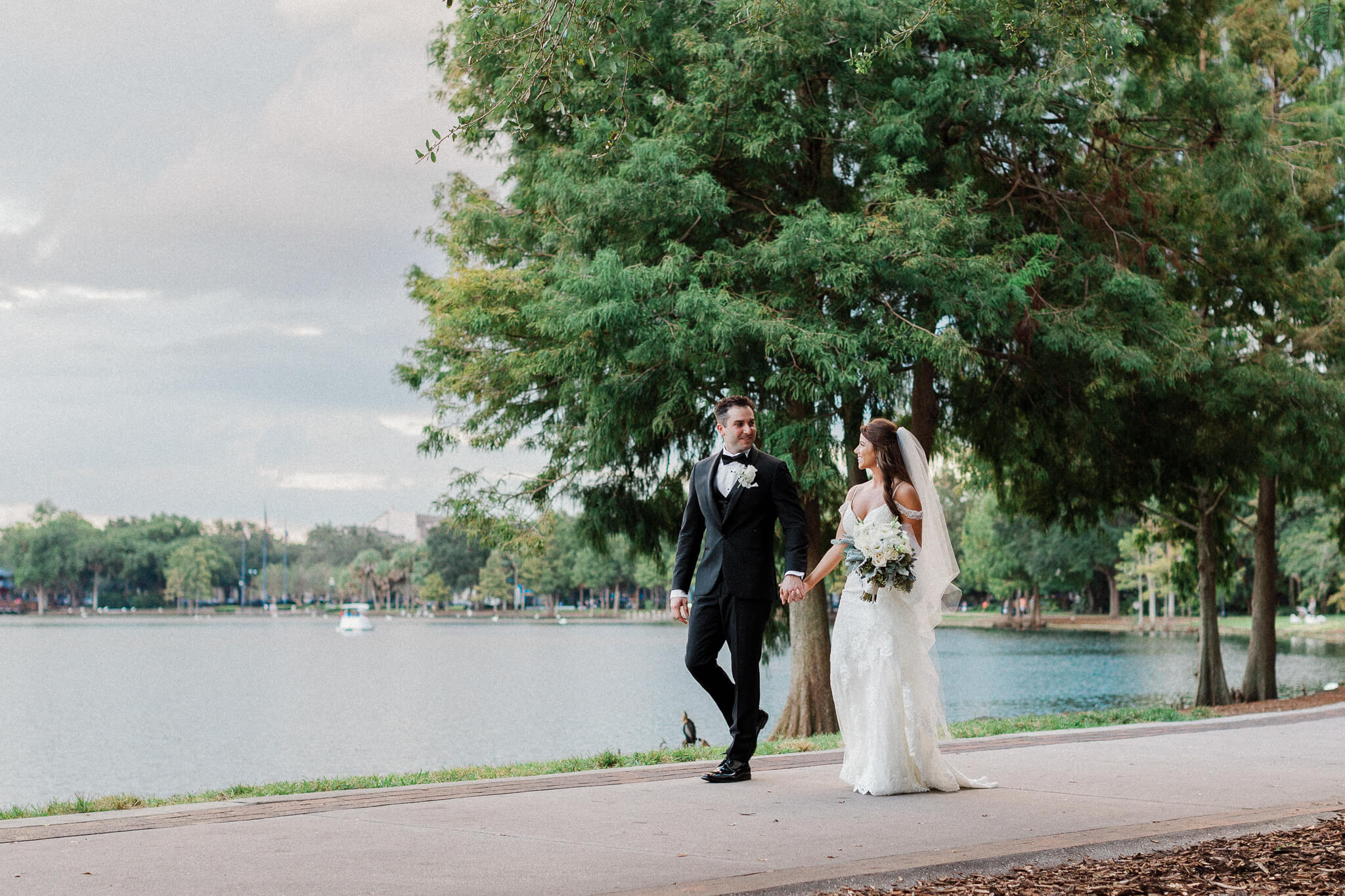 Bride and groom walk together on a path next to a lake