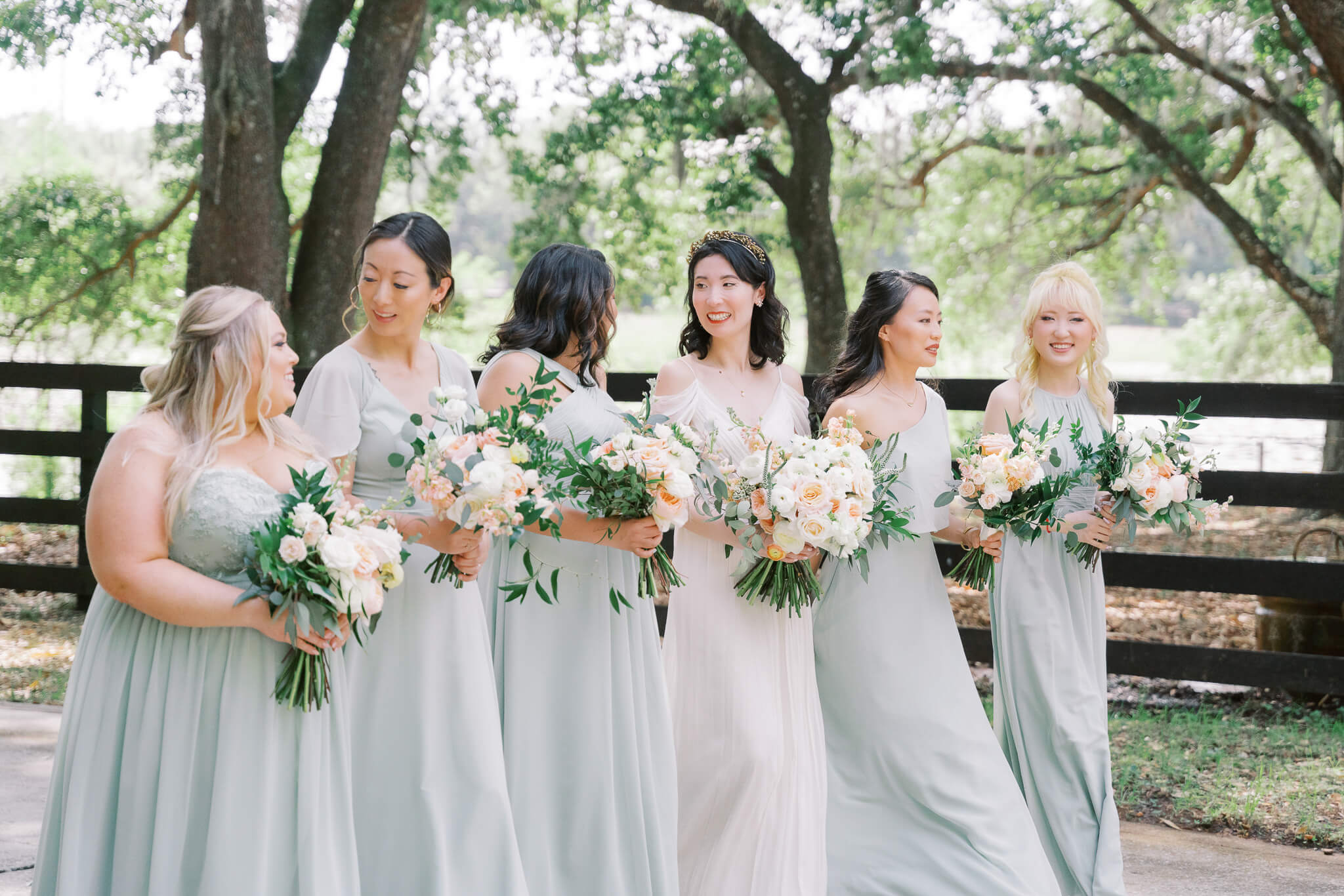 Bride and bridesmaids in sage dresses walk together during a countryside Florida wedding 