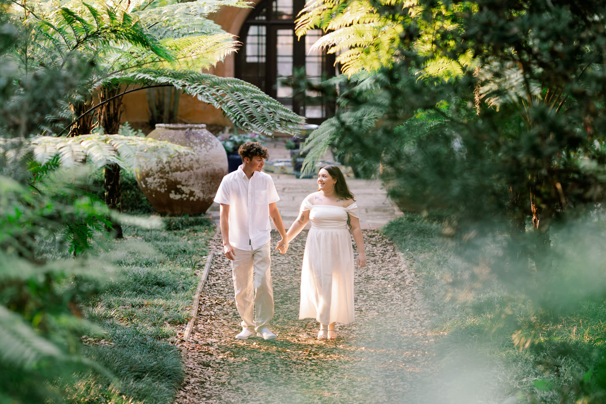 Bride and groom walk in a lush garden while holding hands
