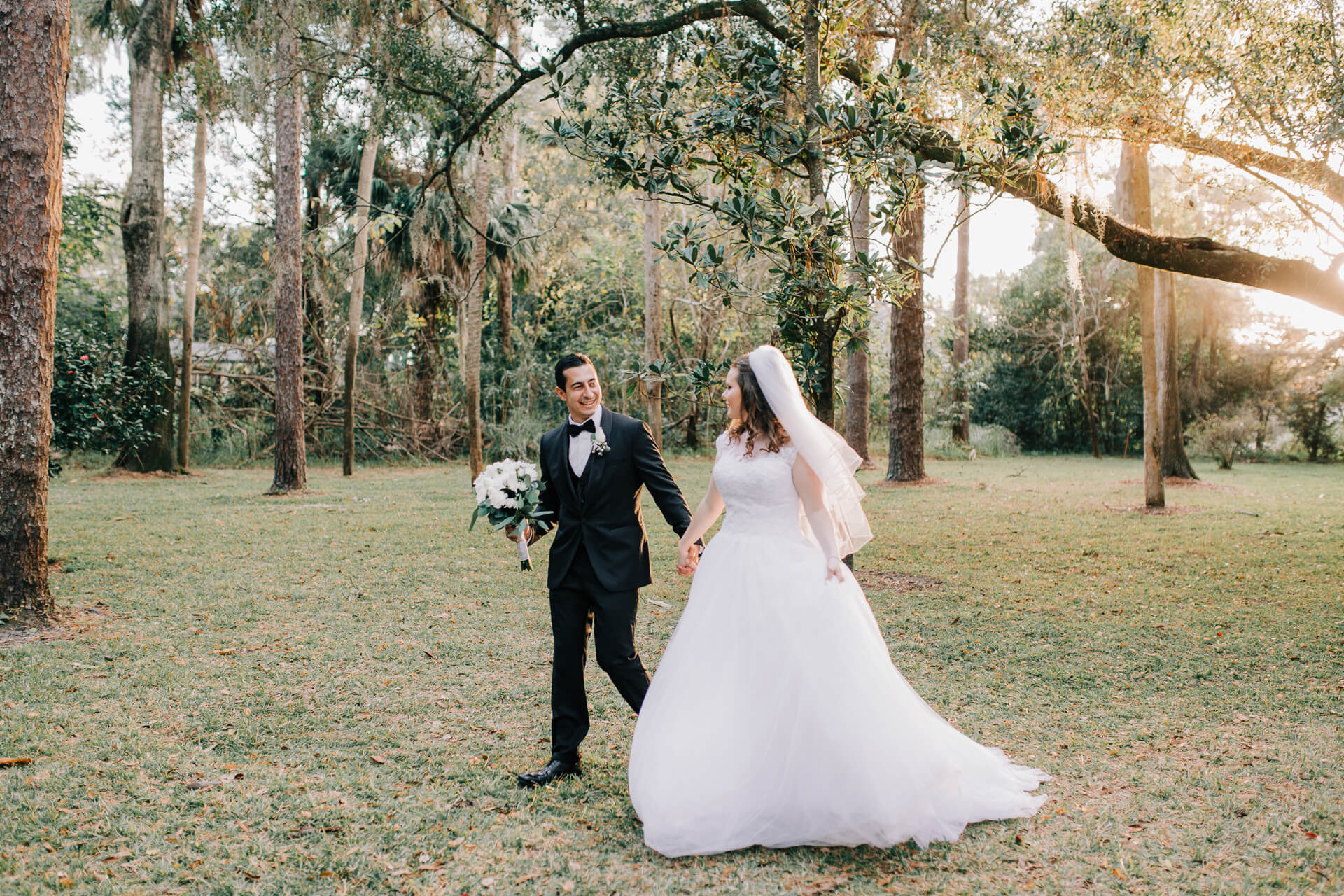 bride and groom walk through a garden with trees during golden hour in a venue for elopements in Orlando