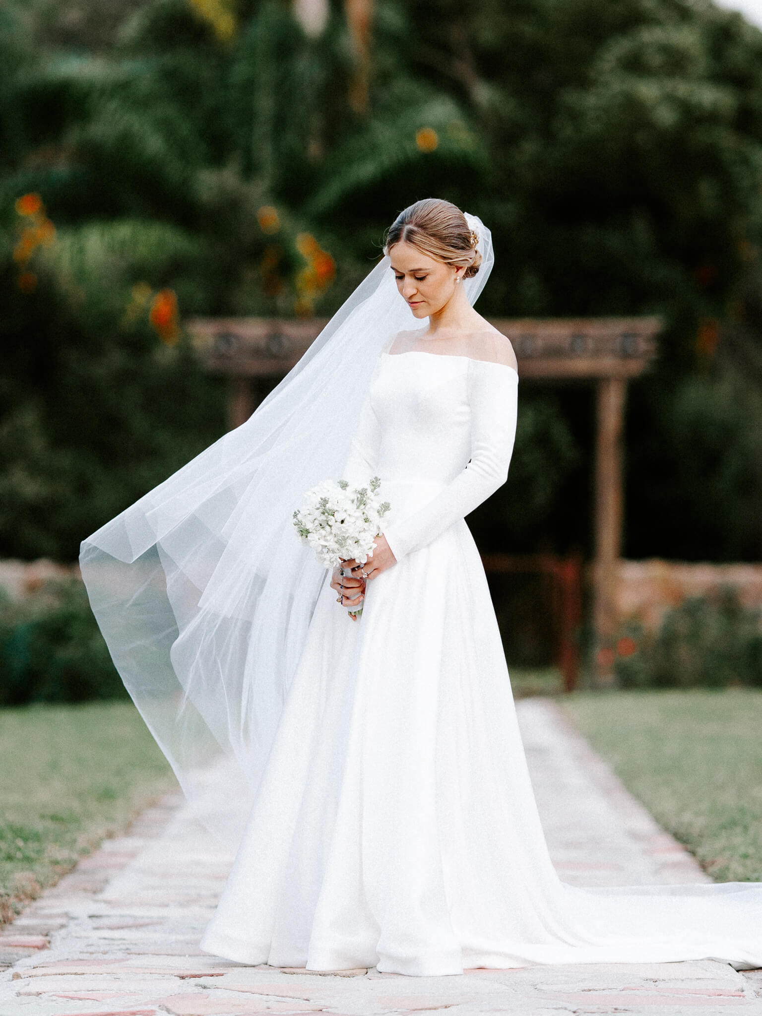 Bride poses for wedding portrait outside the howey mansion while her veil moves with the wind and she looks down at her bouquet