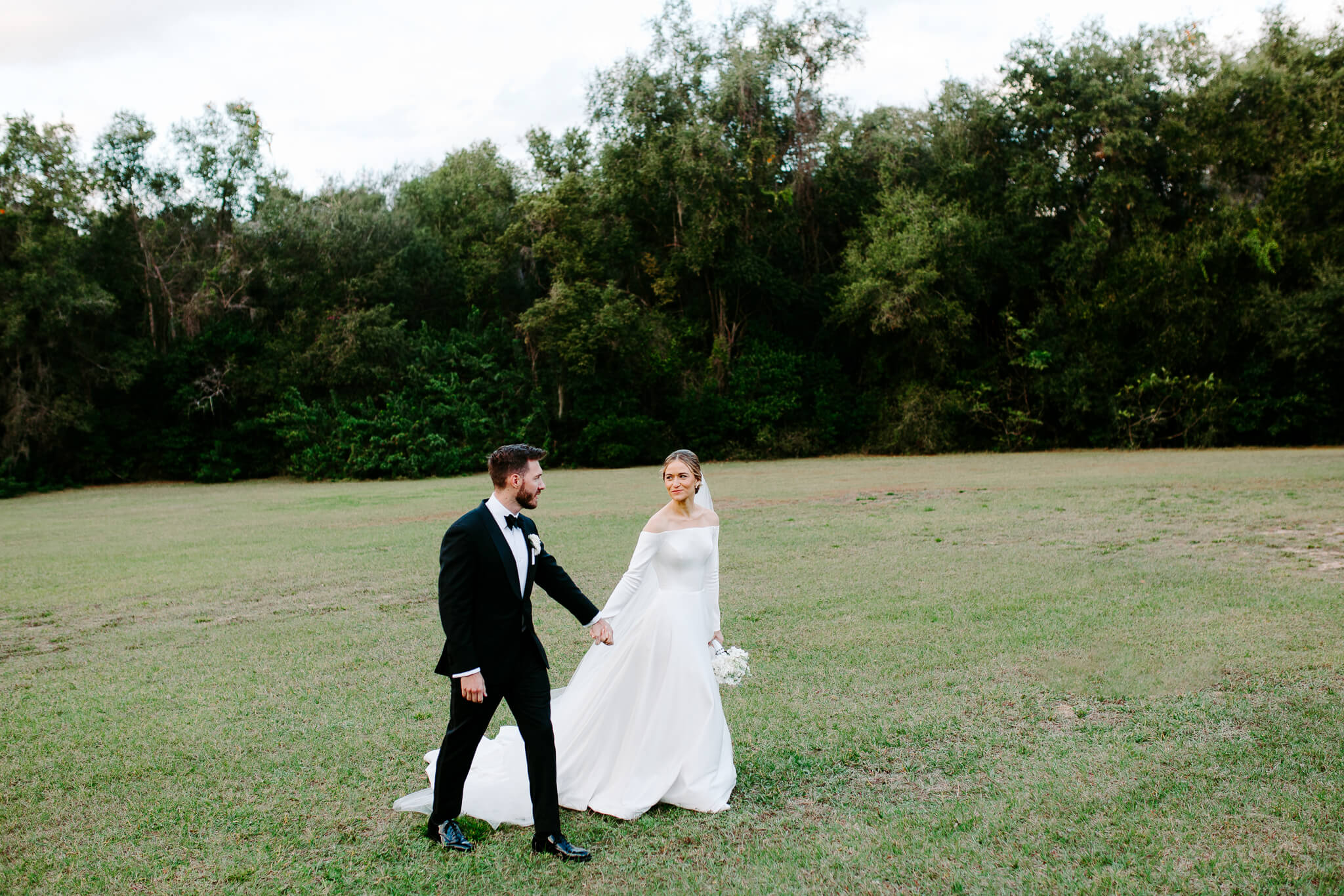 bride and groom hold hands and walk through an open lawn