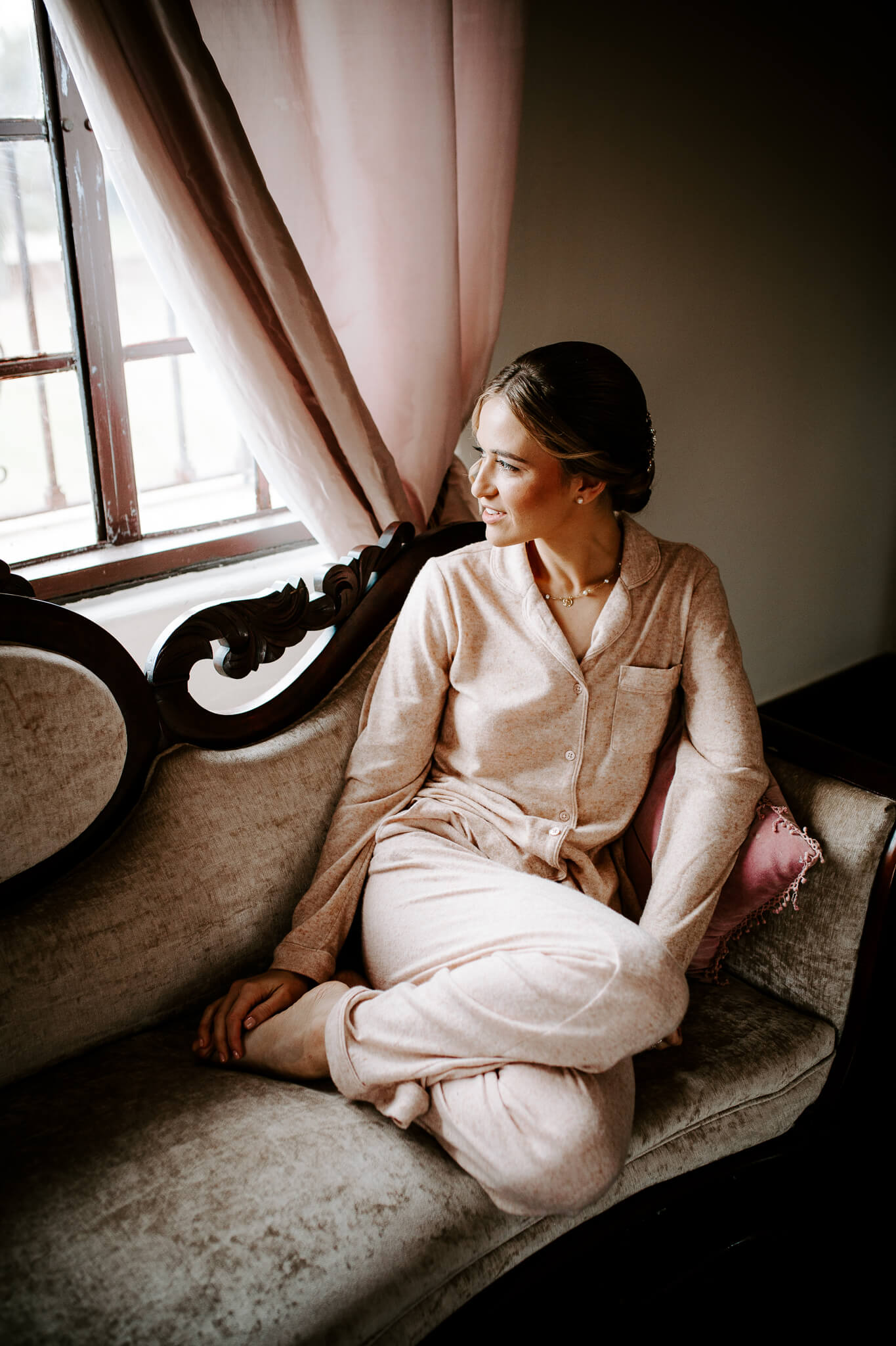 woman in silk pajamas looks out a window