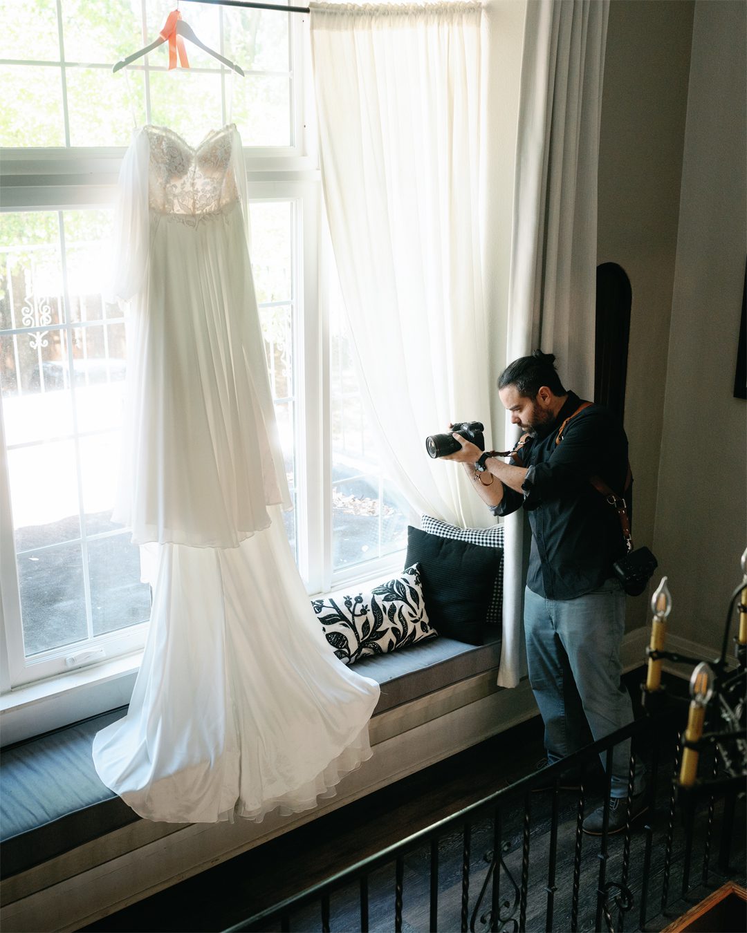 photographer taking photos of a wedding dress that hangs from a window