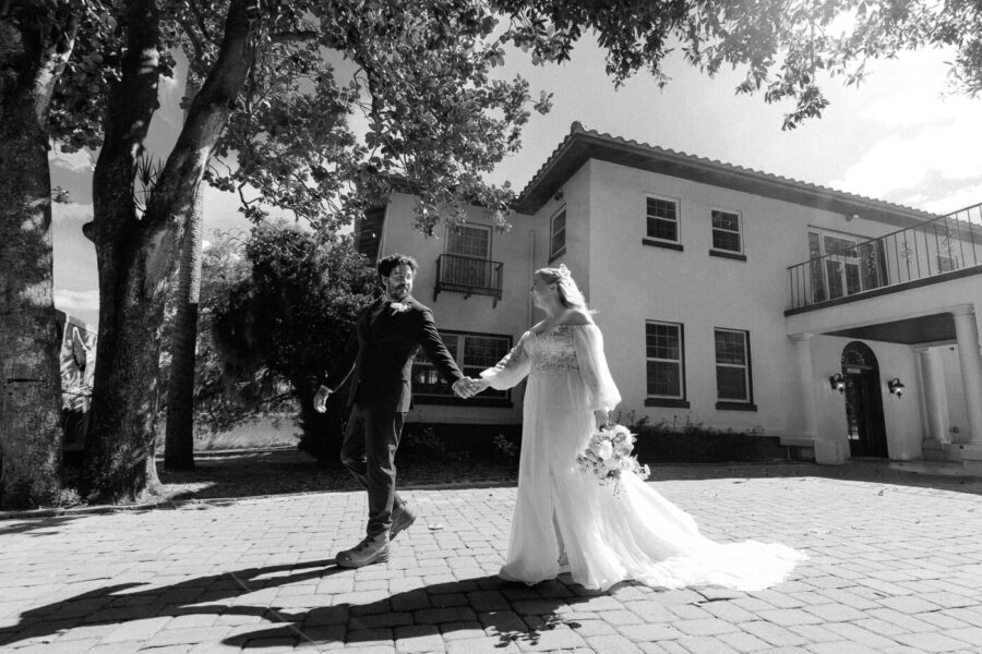 groom and bride hold hands in front of mansion at Lake Lucy Estate wedding venue