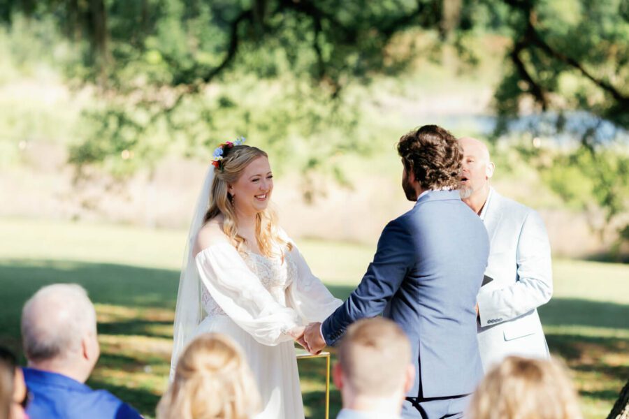 bride and groom hold hands while facing each other during wedding ceremony at Lake Lucy Estate