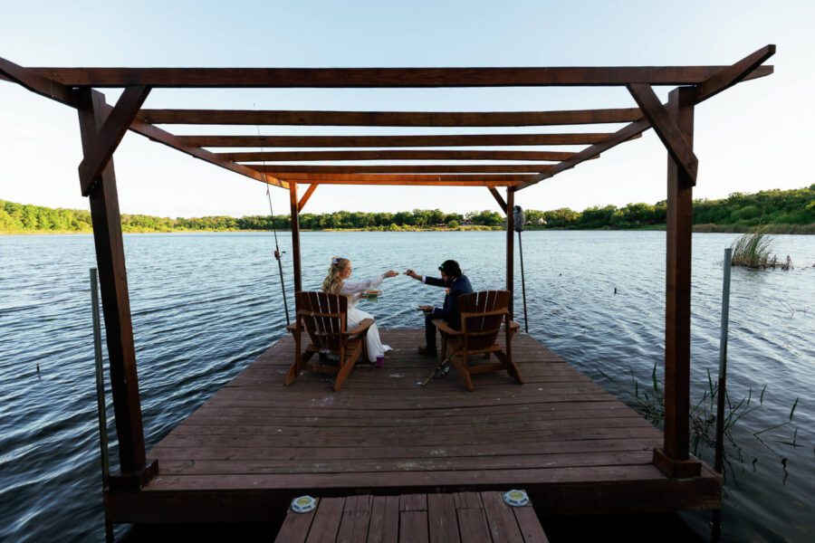 bride and groom sitting in front of a lake while playing with their slices of pizza