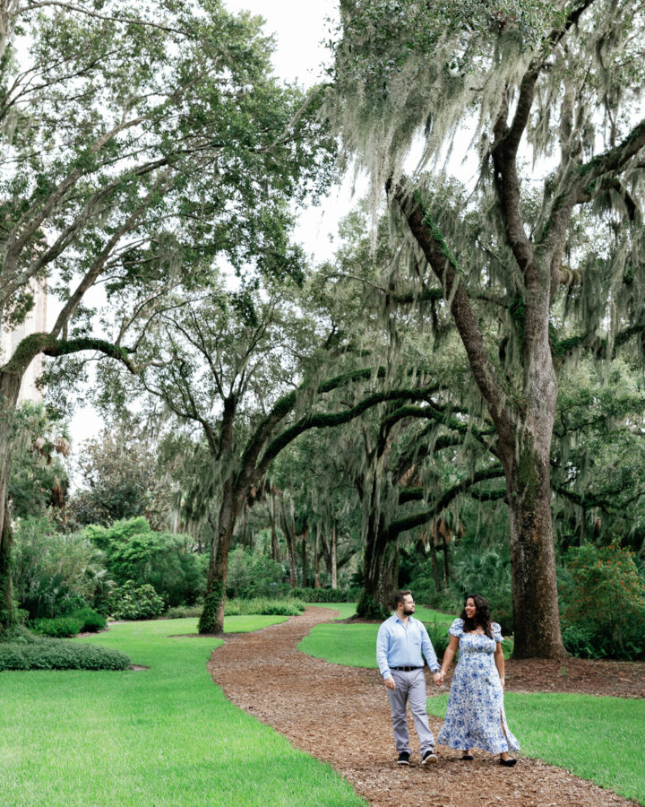 a winding path surrounded by trees at Bok Tower Gardens while a couple walks holding hands after getting engaged